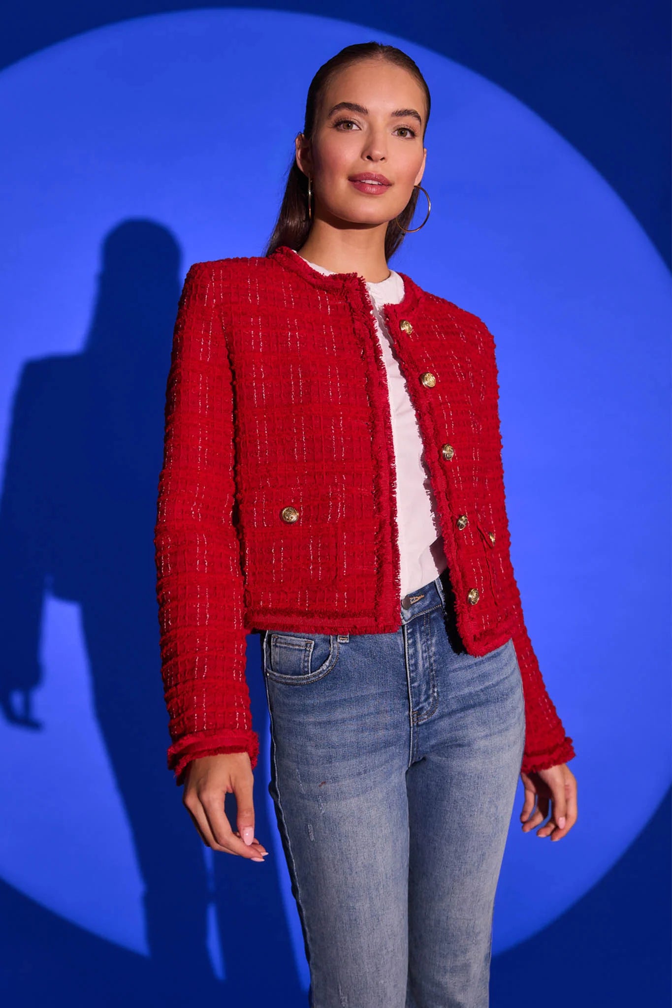 Woman wearing a Evelyn Red Tweed Jacket with gold buttons against a blue background