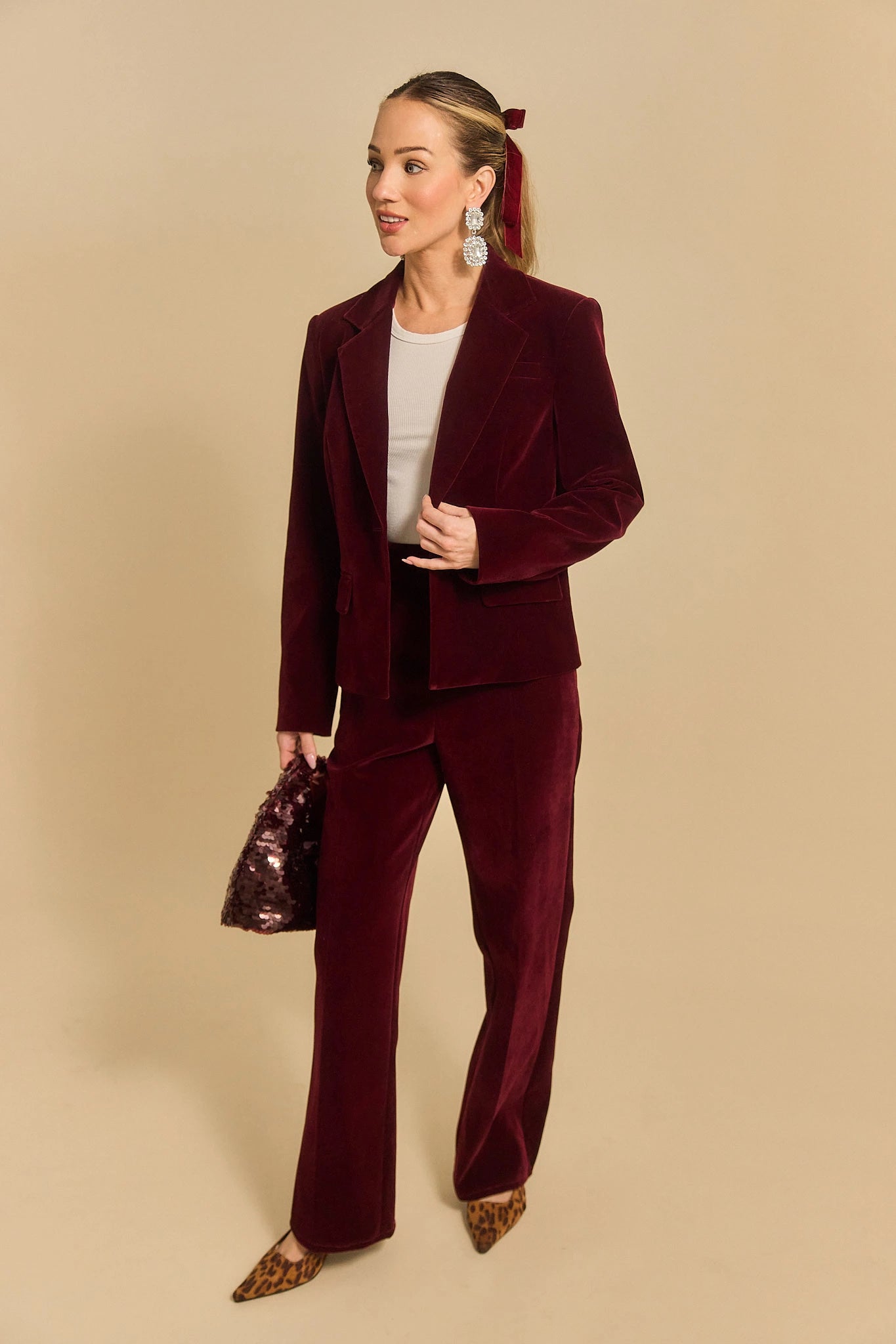 Woman wearing a evie burgundy velvet suit against a beige background