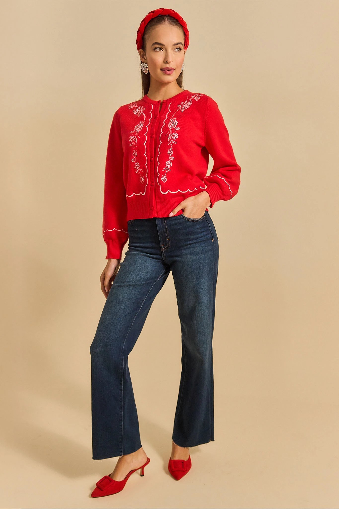 Woman wearing a ginger red embroidered cardigan and blue jeans on a beige background