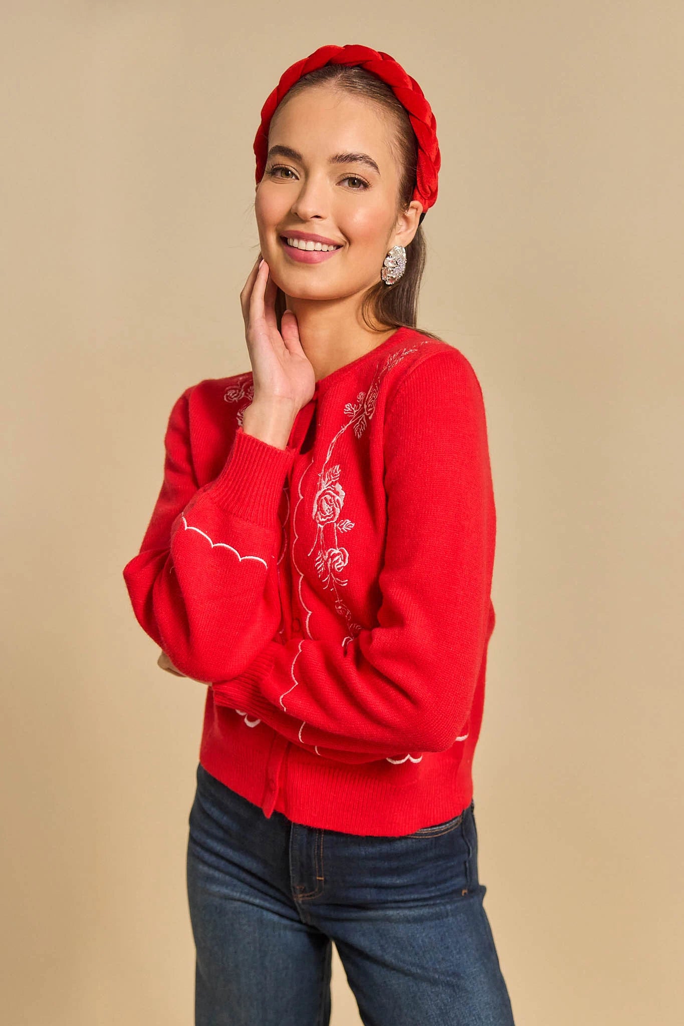 Woman wearing a red ginger cardigan with floral embroidery and a matching headband against a beige background
