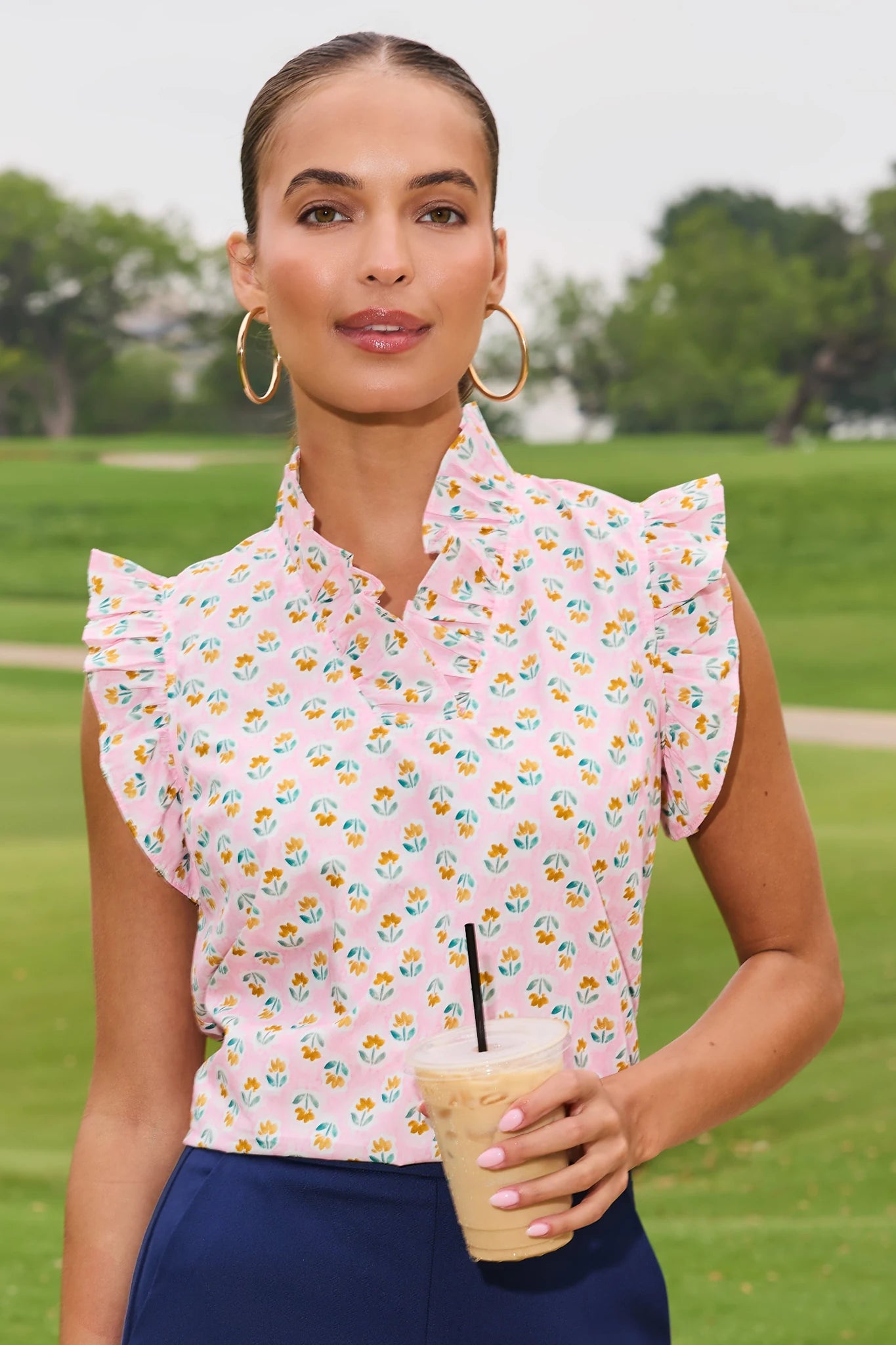 Woman in a floral blouse holding a drink on a grassy field