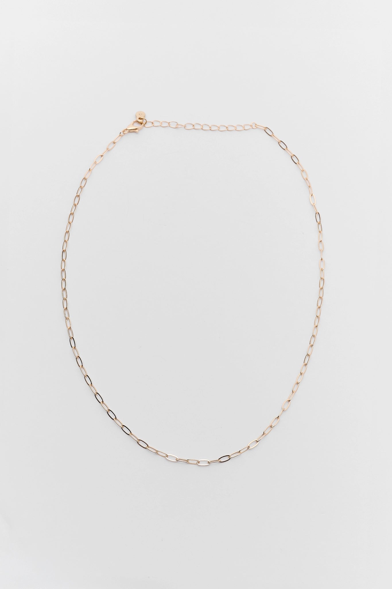 A delicate gold chain necklace with a small oval charm and an adjustable lobster clasp, displayed on a clean white background.