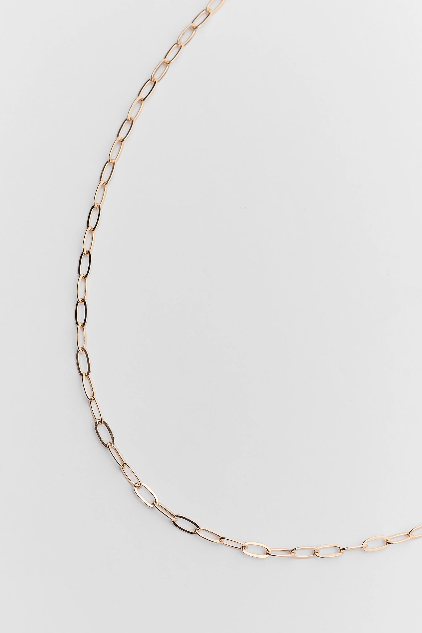 A close up of delicate gold chain necklace with a small oval charm and an adjustable lobster clasp, displayed on a clean white background.