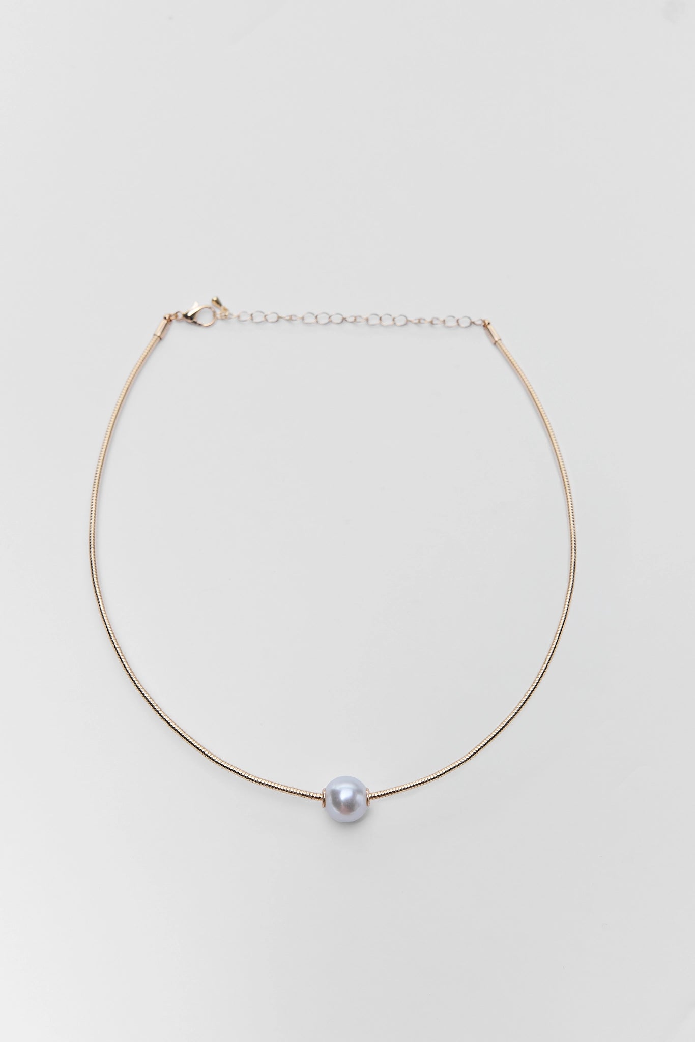 Gold necklace with a single pearl on a light gray background