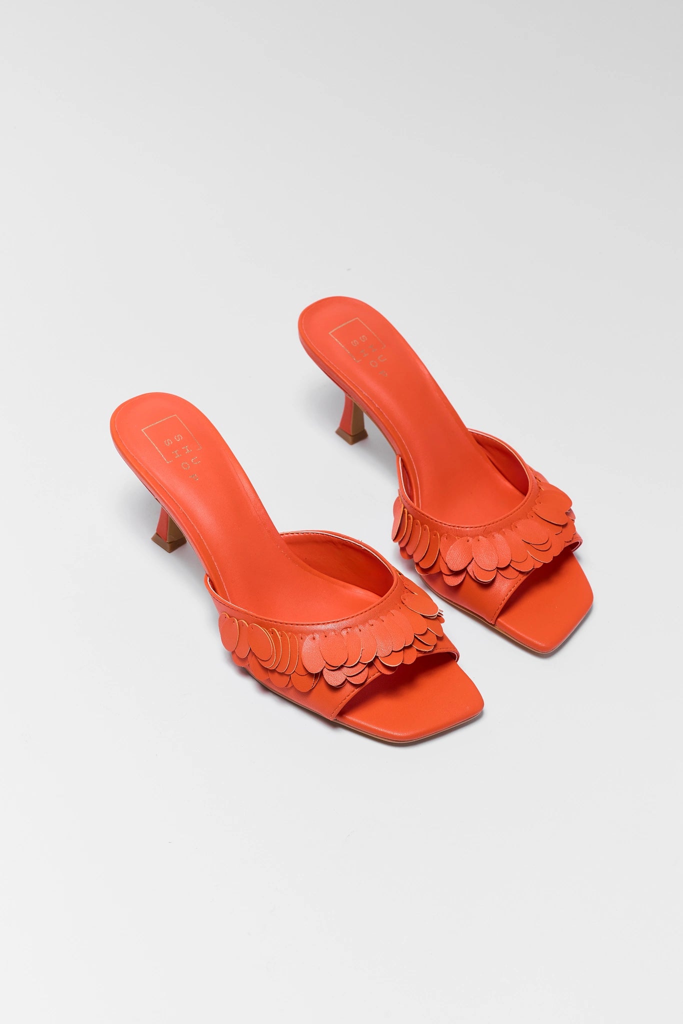 Pair of two orange high-heeled sandals with scalloped edges on a light gray background