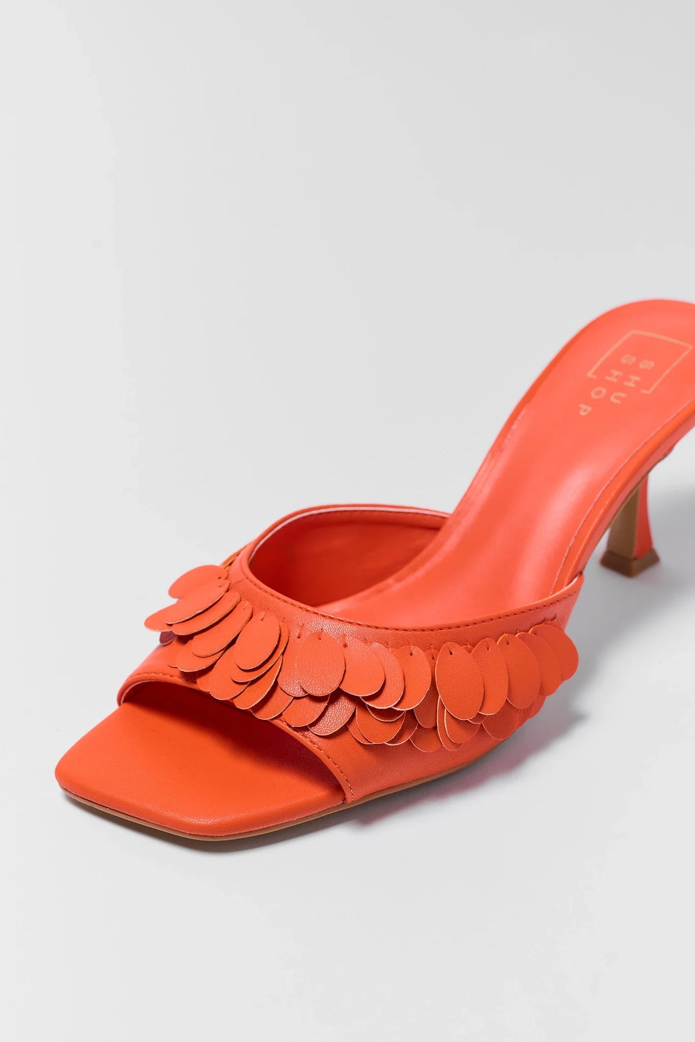 detailed Orange high-heeled shoe with floral details on a light gray background