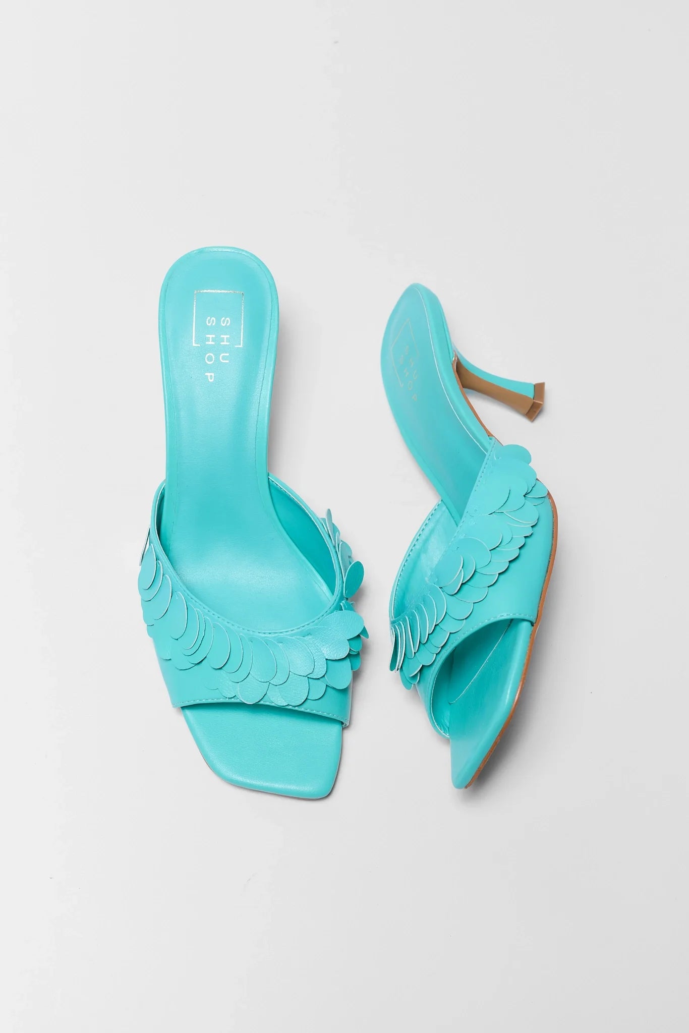 Pair of turquoise high-heeled shoes with ruffled details on a light gray background