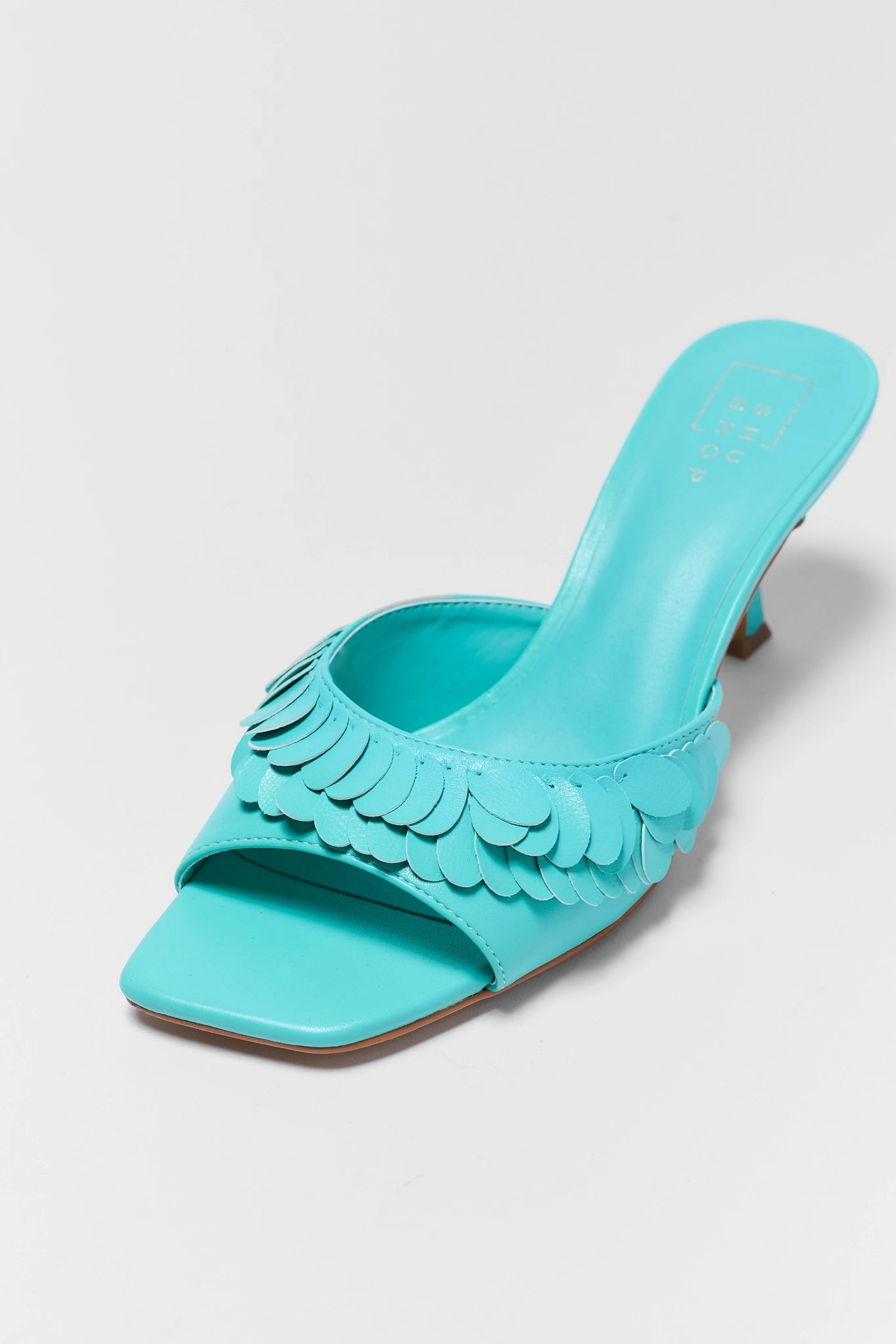 Turquoise sandal with decorative scalloped edge on a light gray close background
