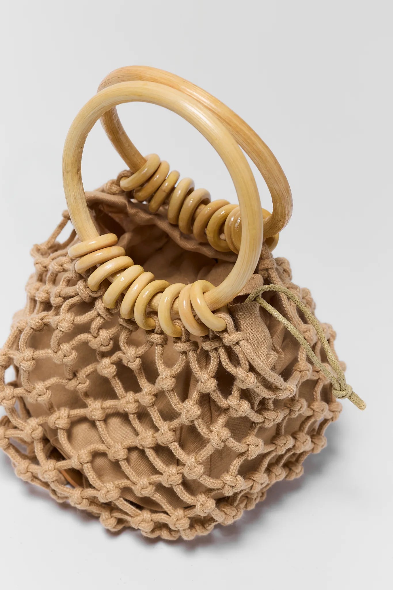 Beige woven handbag with wooden handle on a white background