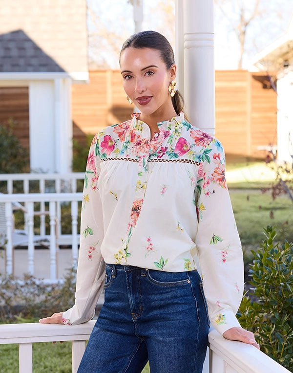 Woman wearing a floral blouse and blue jeans standing outdoors.