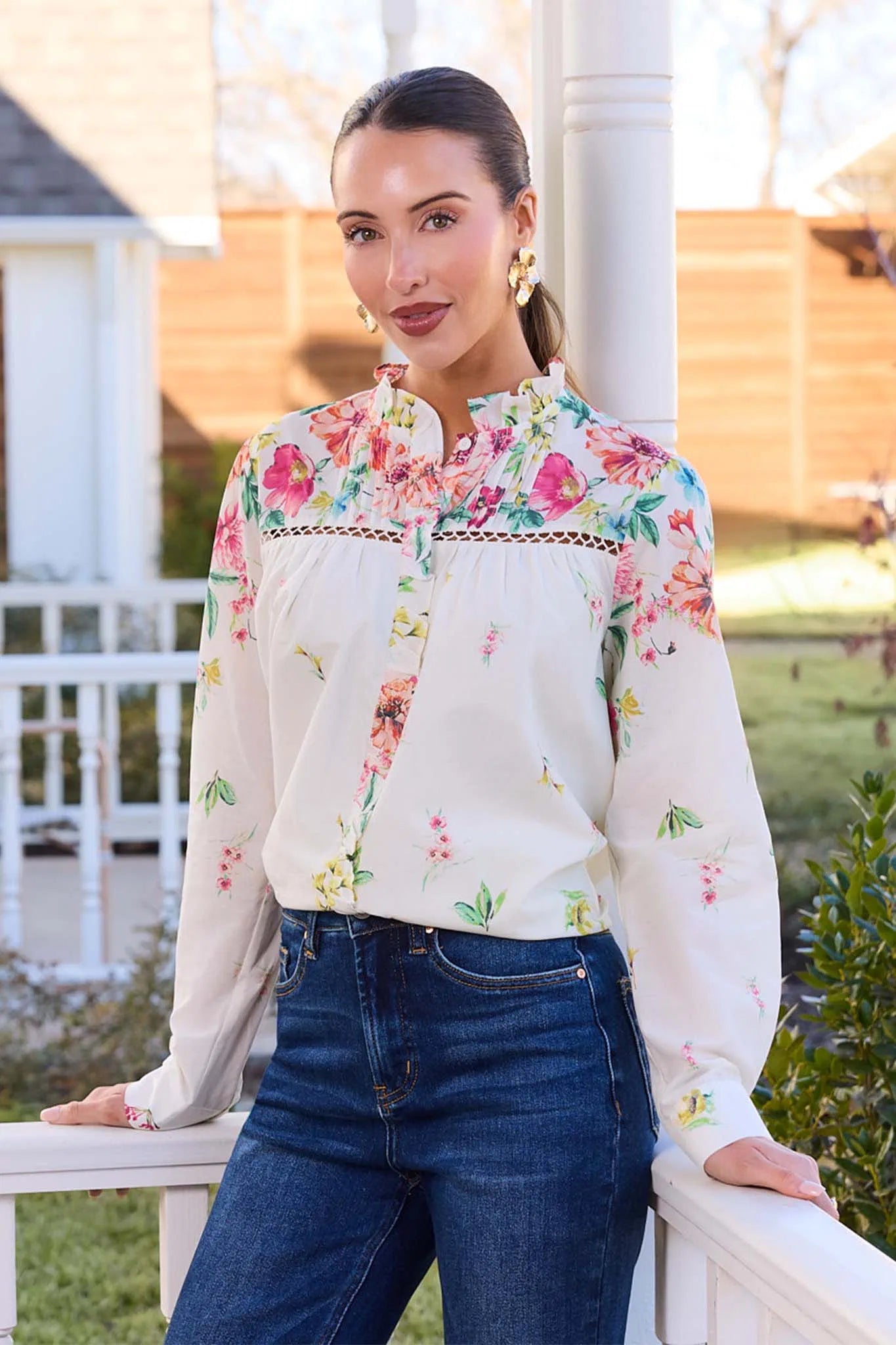 Woman wearing a floral blouse and jeans standing outdoors.