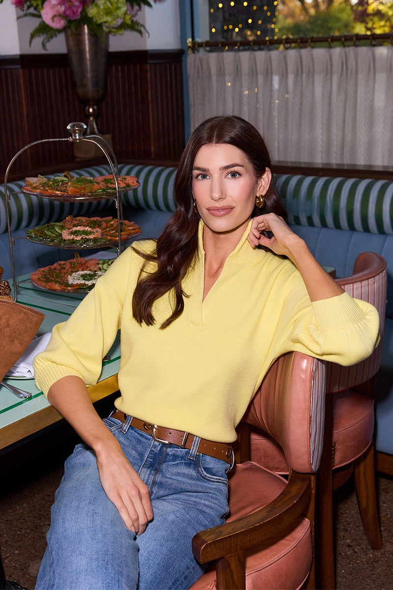 Woman in a yellow sweater and blue jeans sitting in a restaurant.