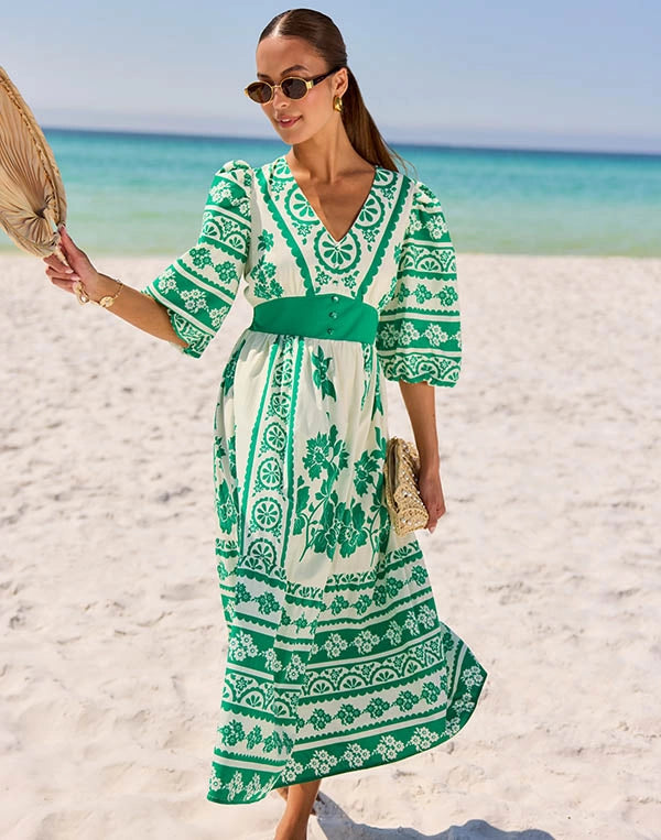 Woman in a green and white patterned dress on a beach nav