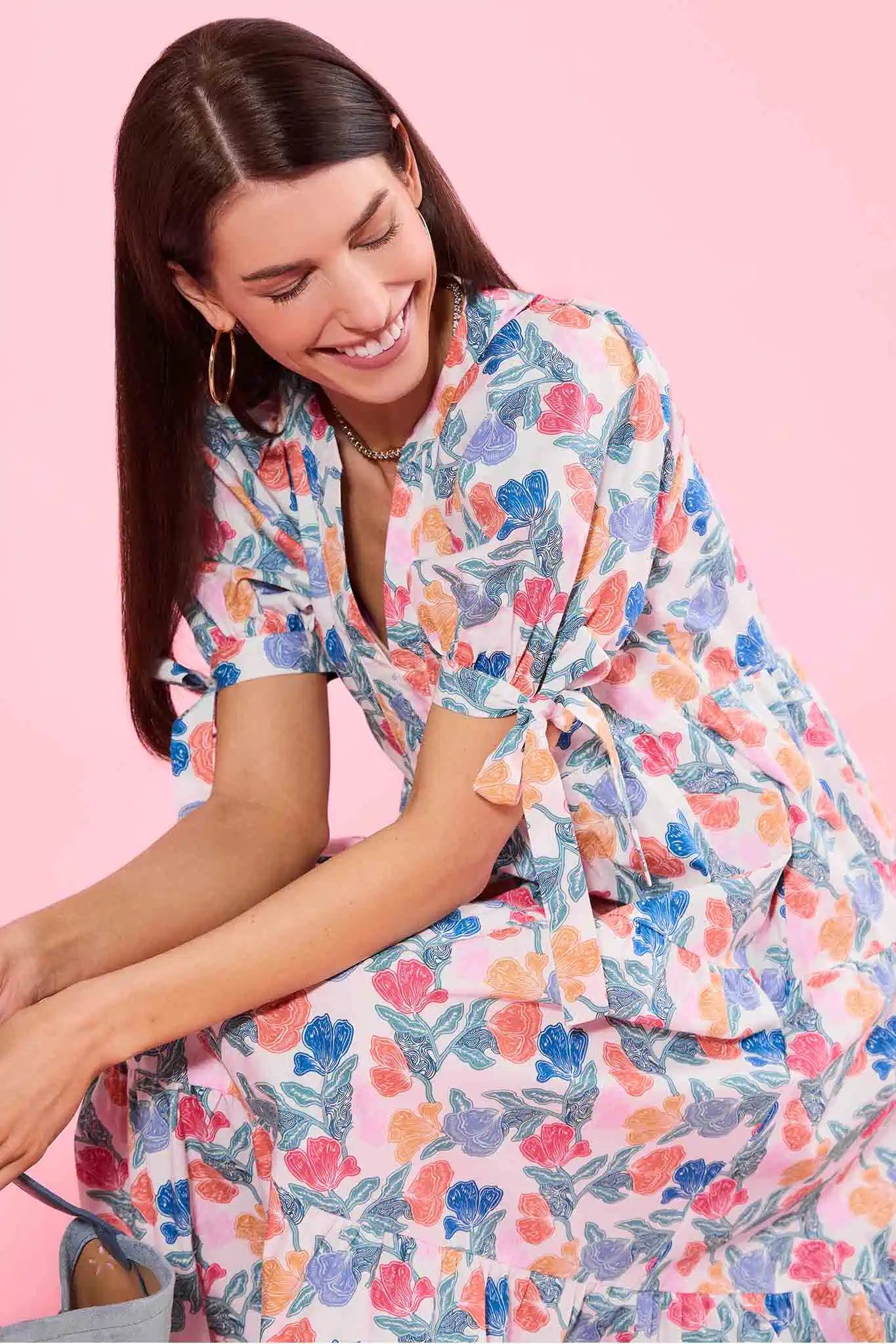 Woman wearing a colorful floral dress against a pink background
