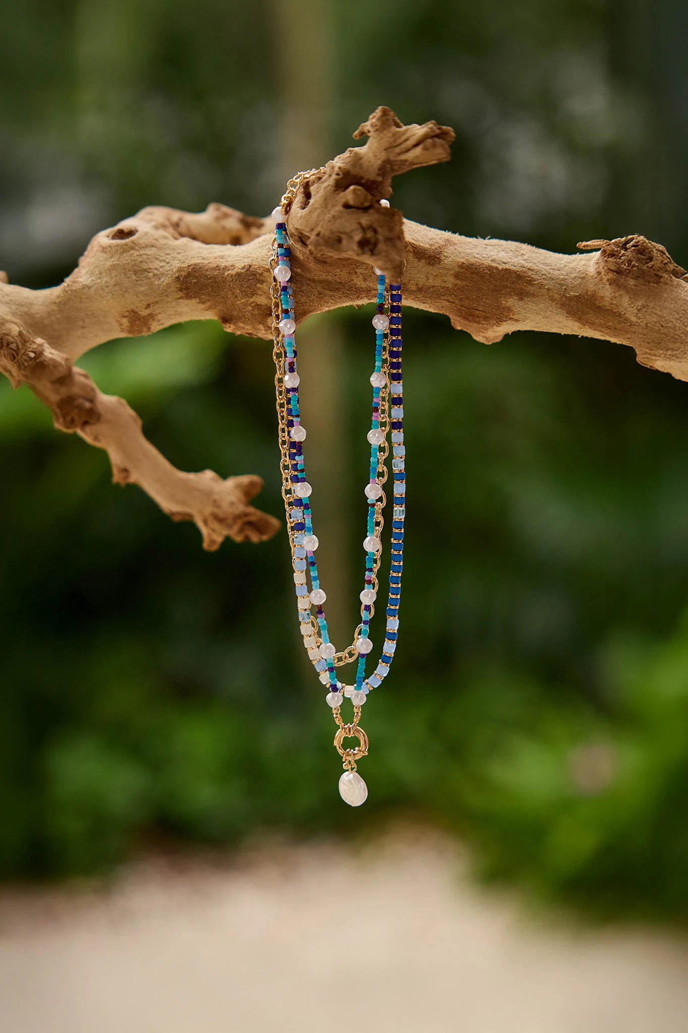 Beaded necklace with a pendant hanging on a branch with a blurred green background