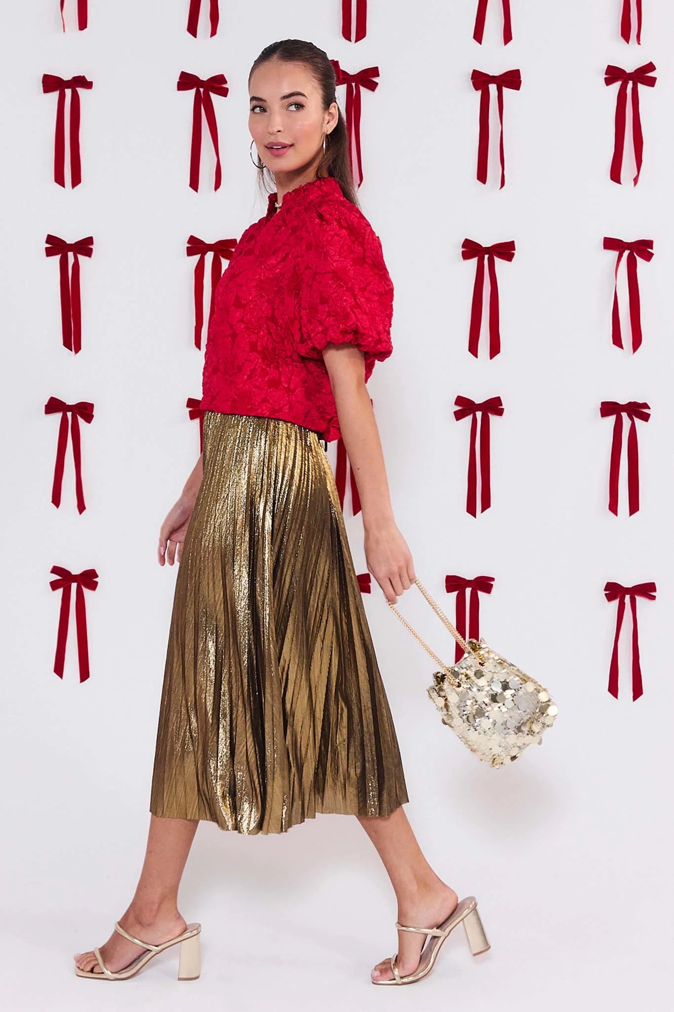 Woman wearing a red top and gold skirt with a white background and red bow pattern