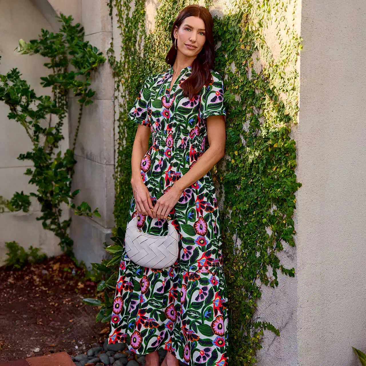 Woman in a floral dress standing against a wall with greenery