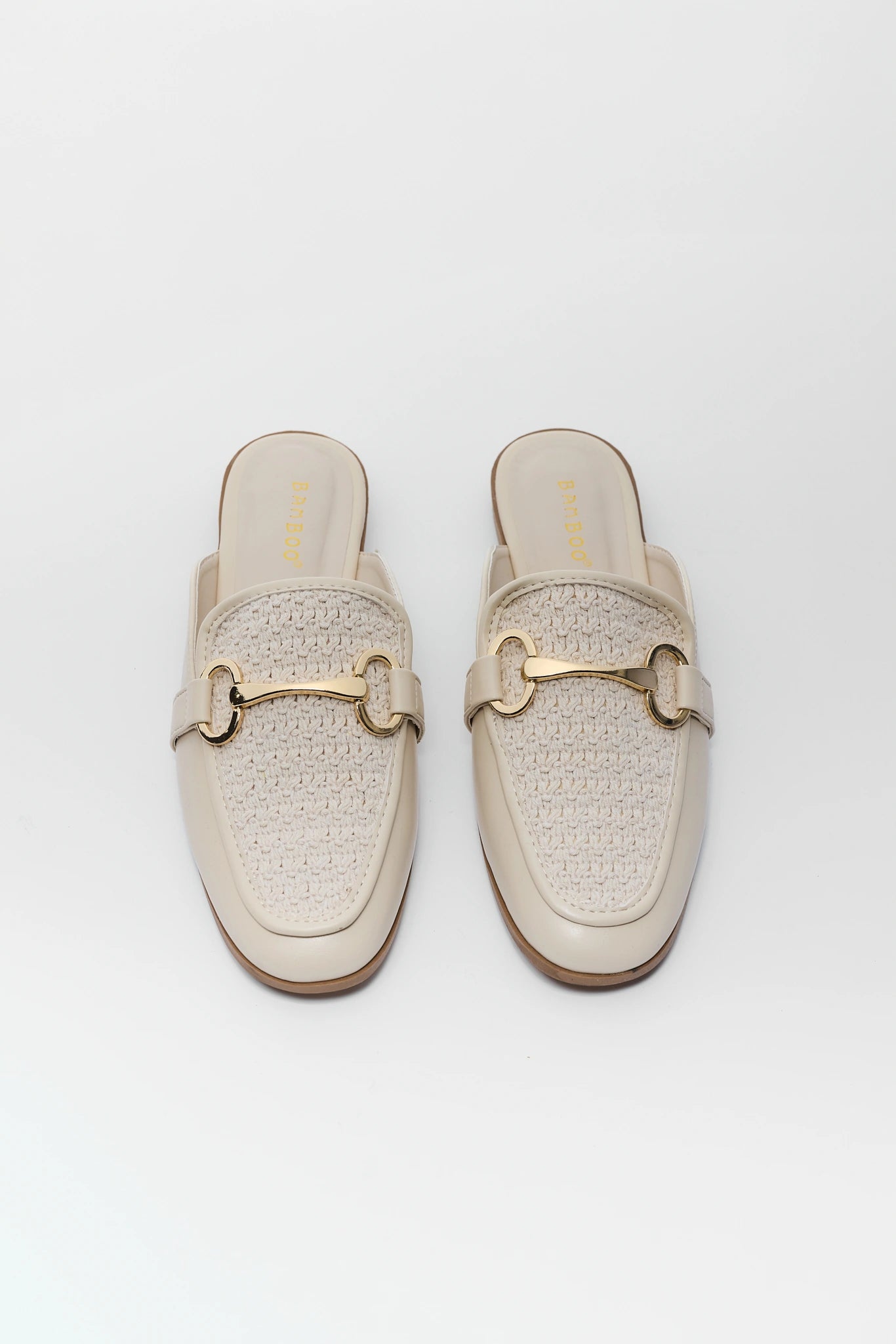 Pair of beige woven slip-on shoes with gold accents on a background