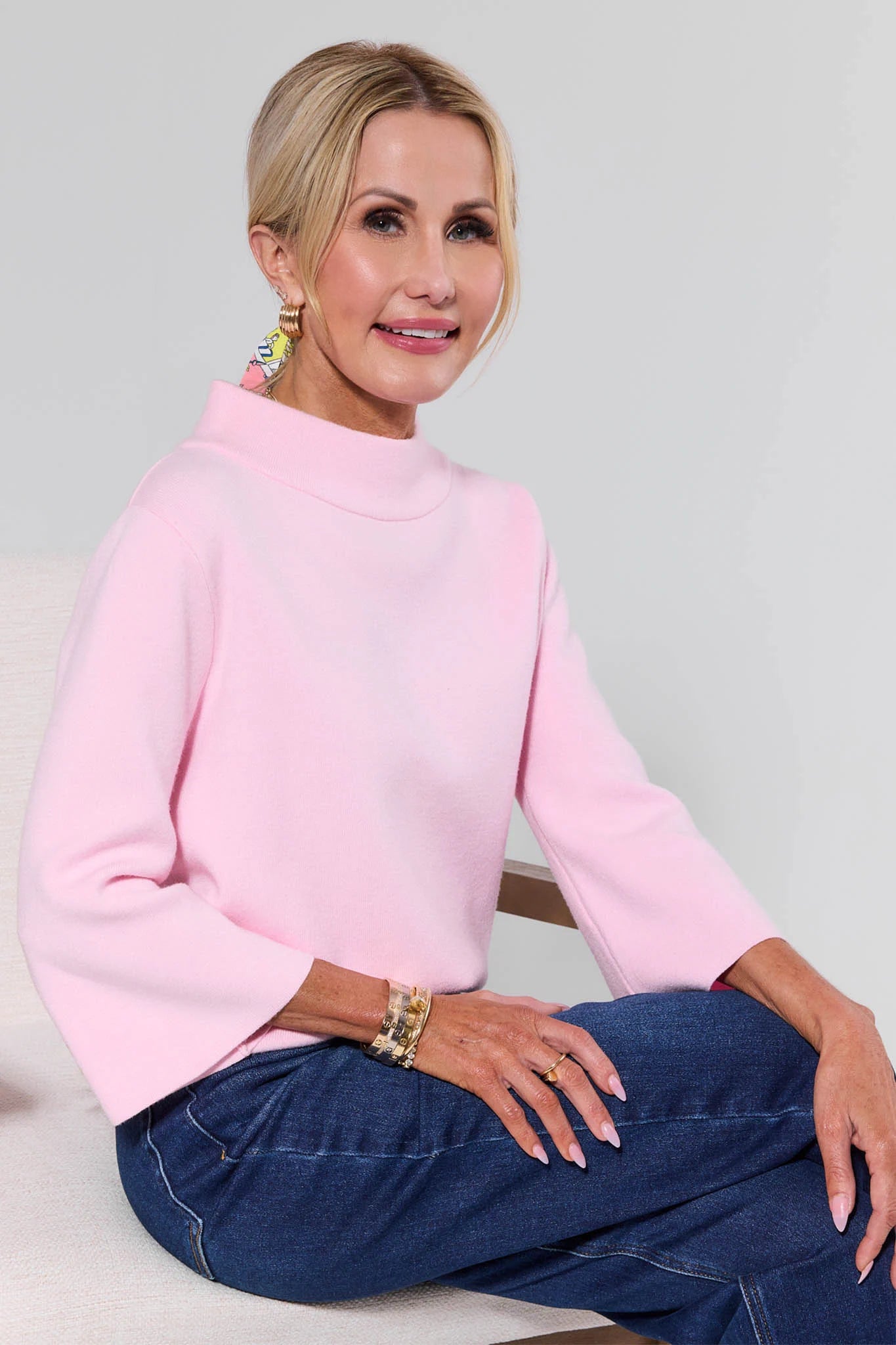Woman wearing a pink sweater and blue jeans against a plain background