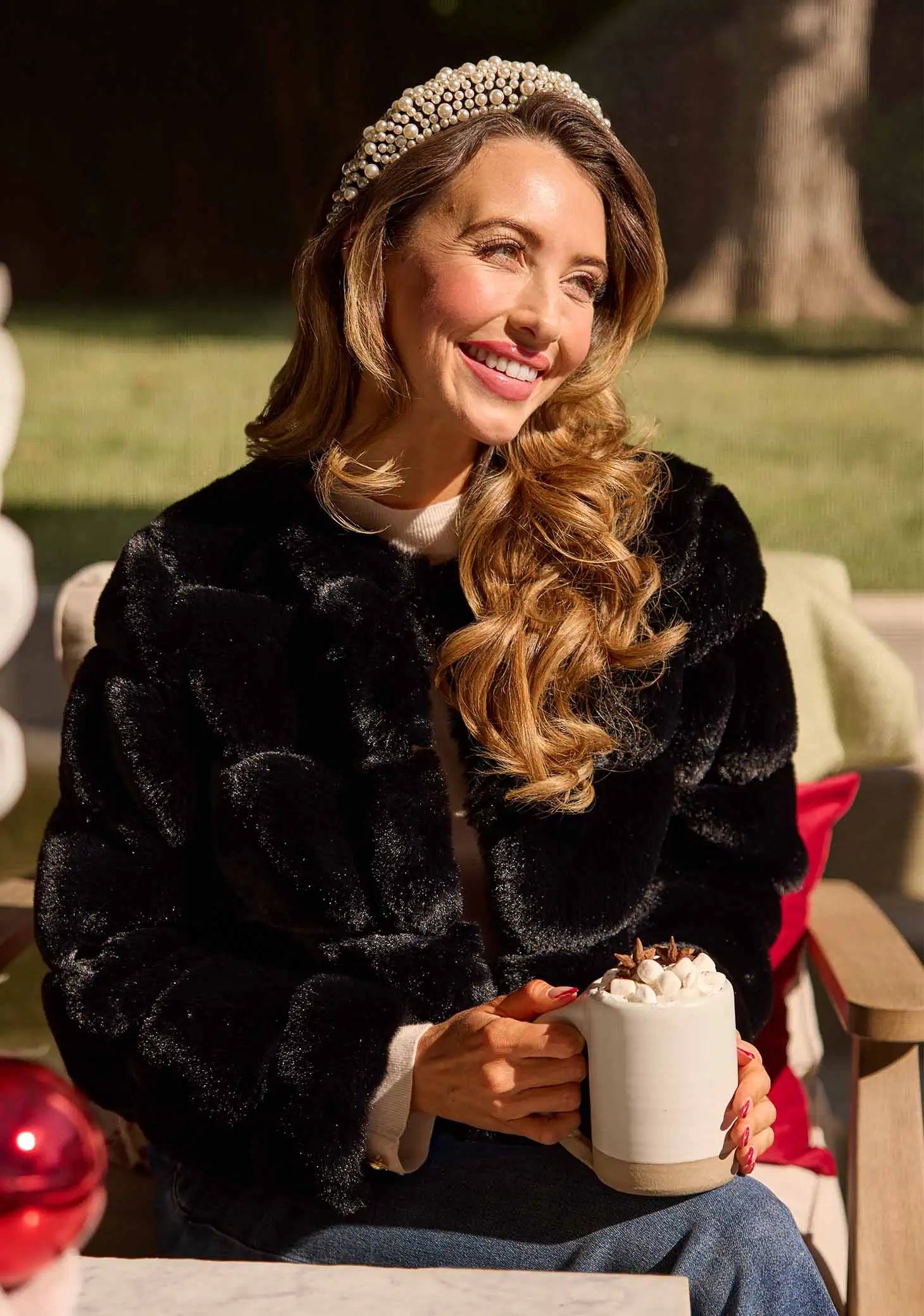 Woman in a black fur coat holding a hot chocolate mug outdoors.