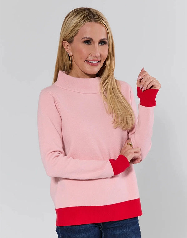 Woman wearing a pink sweater with red cuffs and hem on a gray background