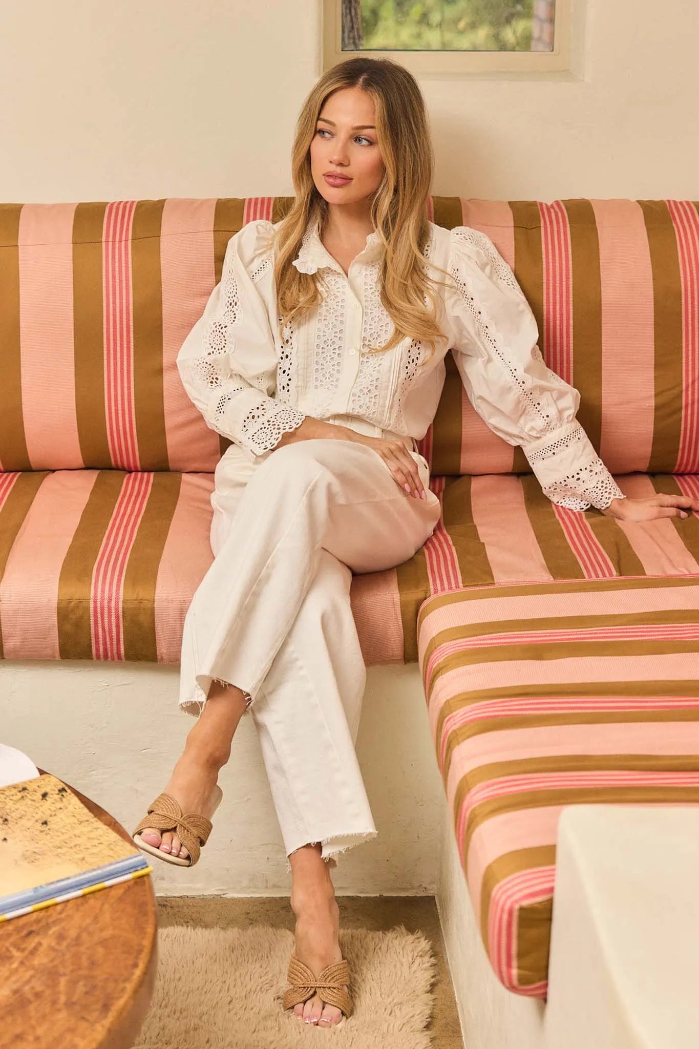 Woman sitting on a striped sofa wearing a white outfit.