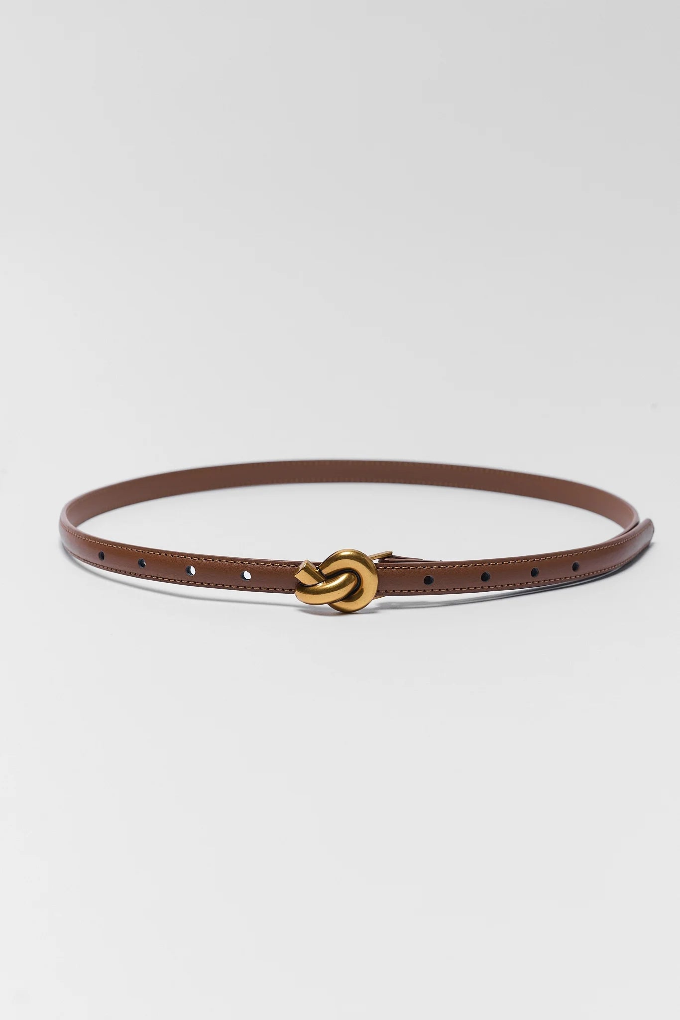 A slim brown leather belt with a distinctive interlocking knot buckle in polished gold-tone metal, displayed on a clean light gray background.