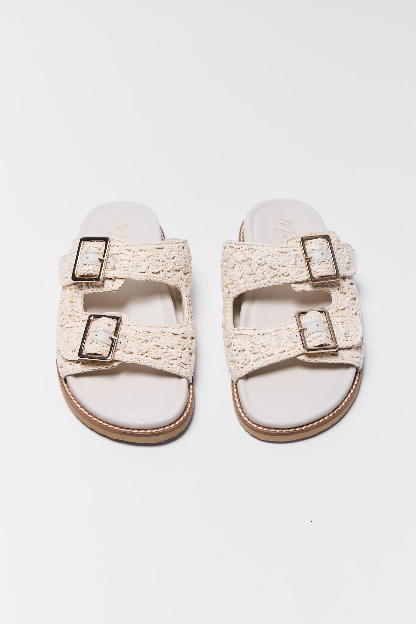 Two beige sandals with buckles on a light gray background