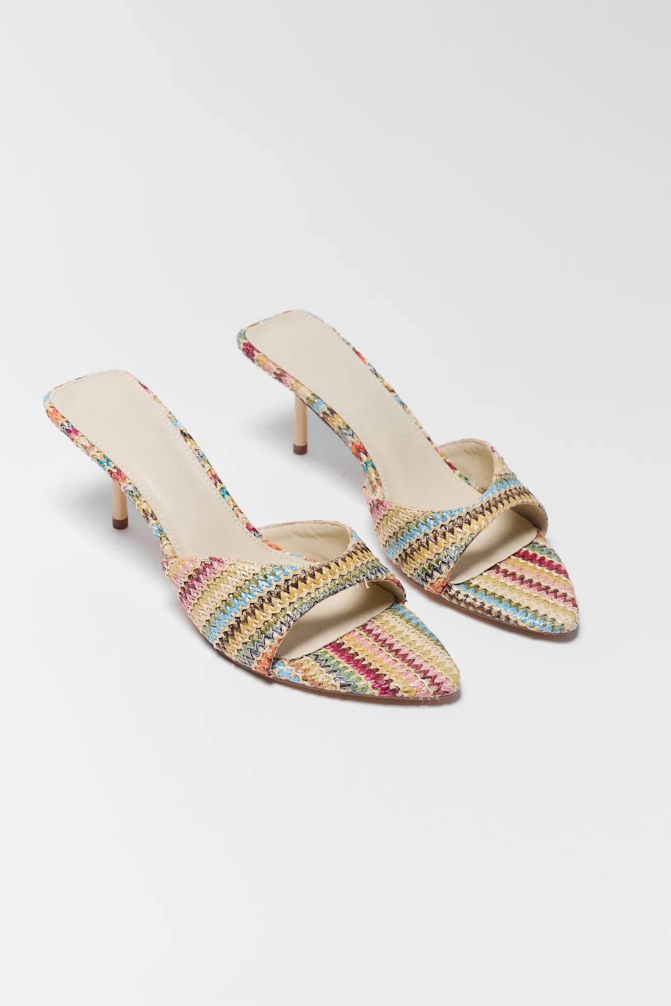 Pair of multicolored woven high-heeled shoes on a white grey background