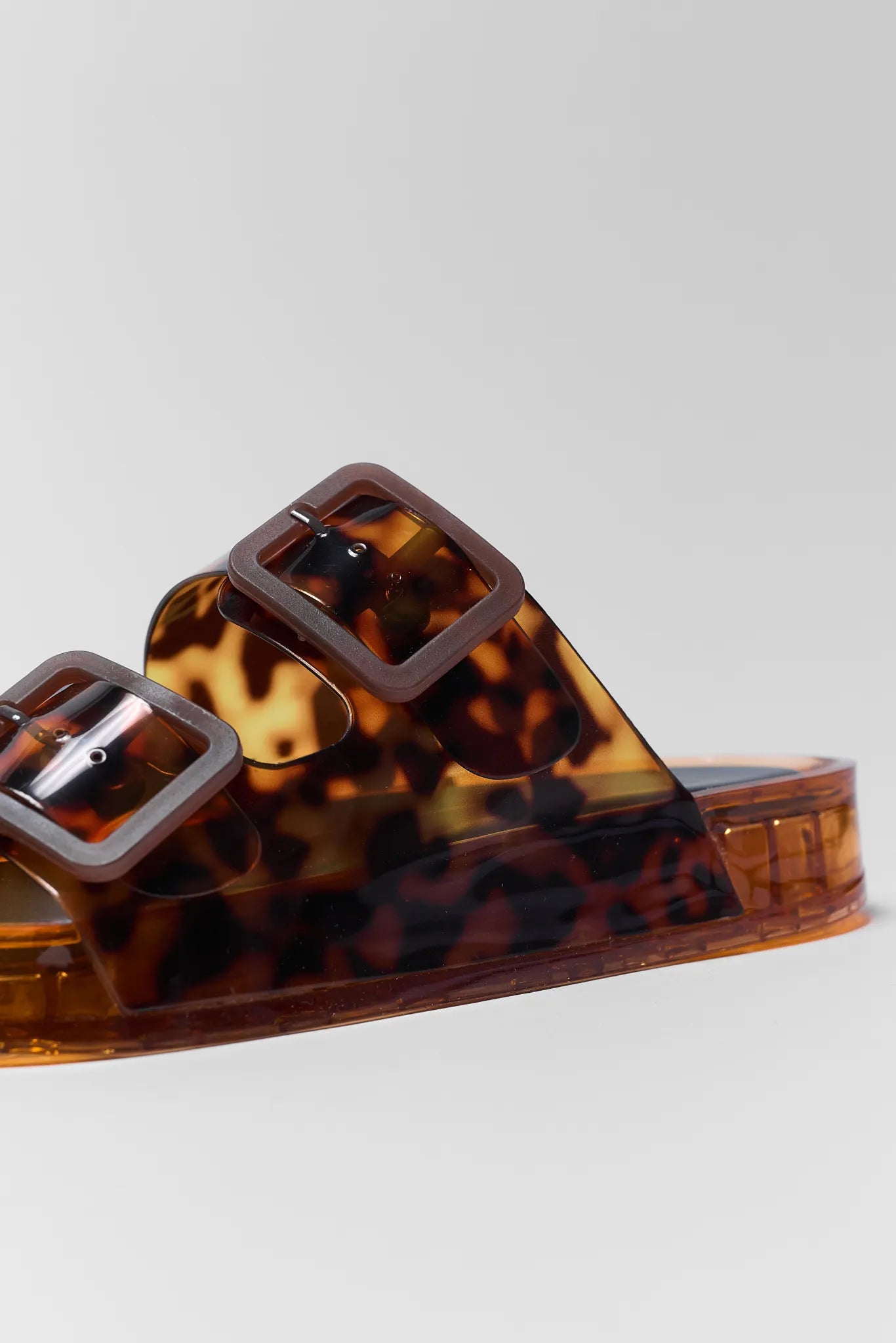 Tortoiseshell sandal with a clear strap on a light gray background