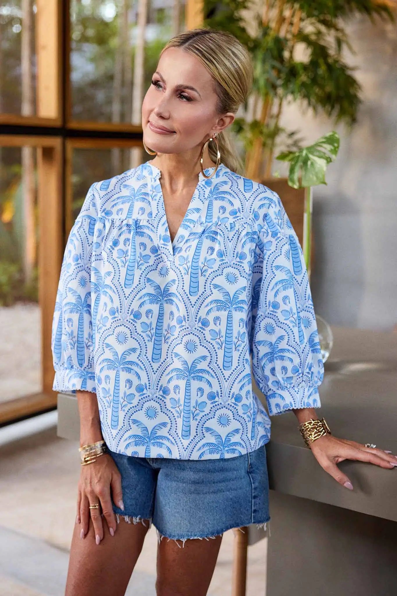 Woman wearing a blue patterned blouse and denim shorts in an outdoor setting.