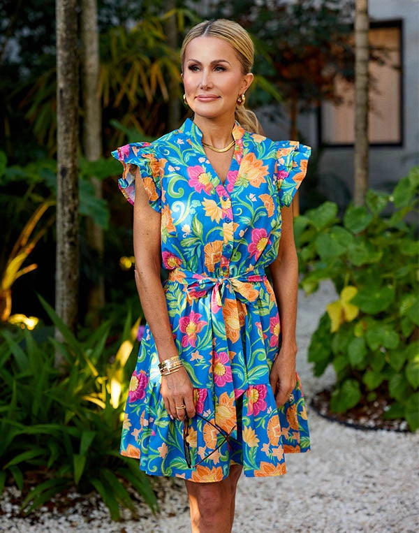 Woman wearing a colorful floral dress standing outdoors with greenery in the background