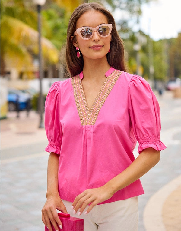 Woman wearing a pink blouse with intricate detailing in an outdoor setting