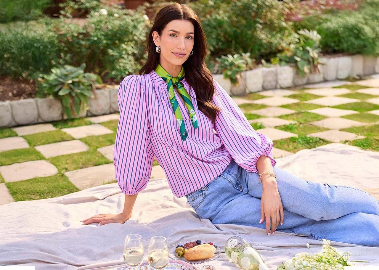 Woman in a garden setting wearing a striped blouse and sitting on a blanket with a picnic setup.