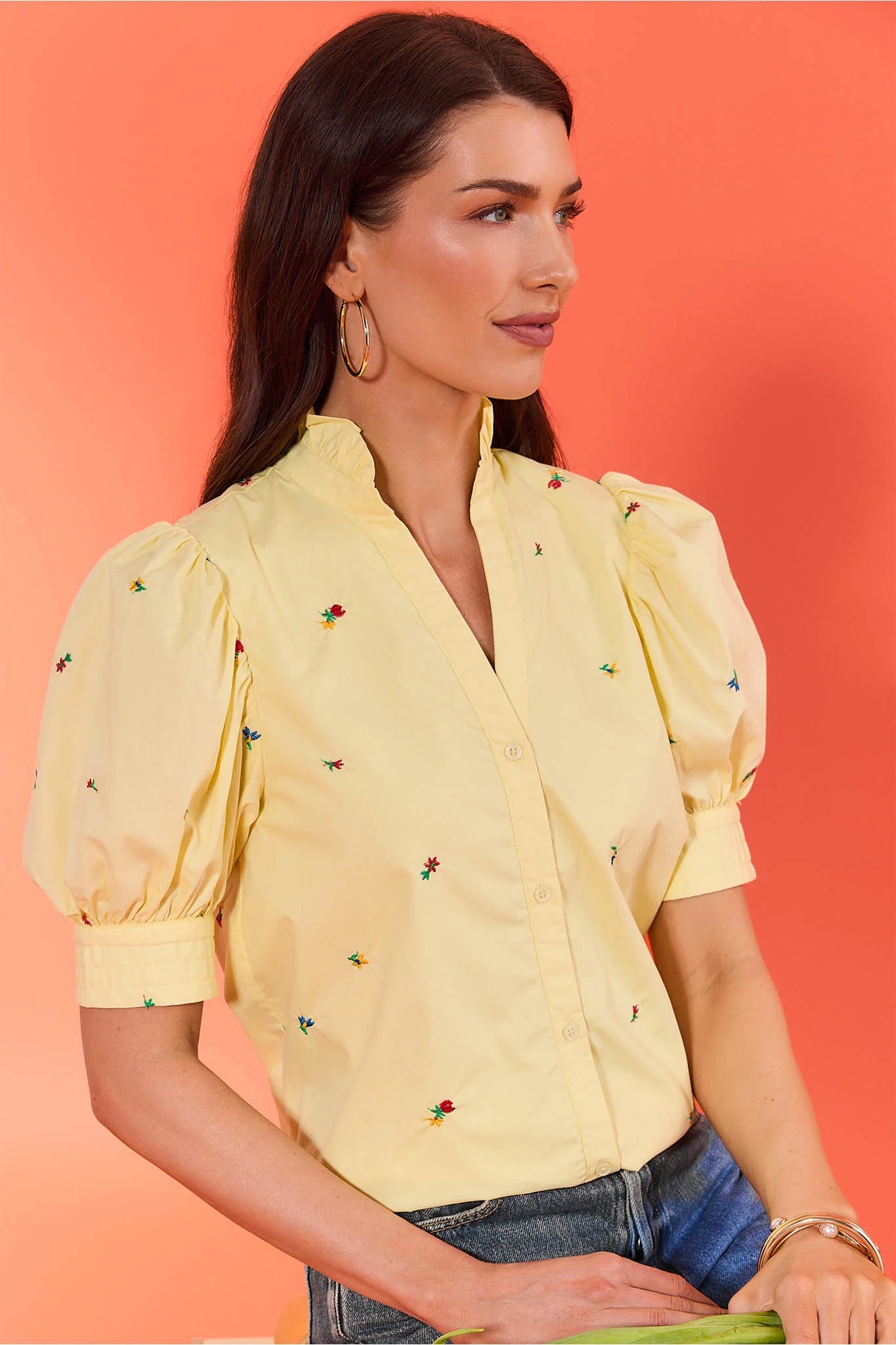Woman wearing a yellow blouse with floral embroidery against an orange background