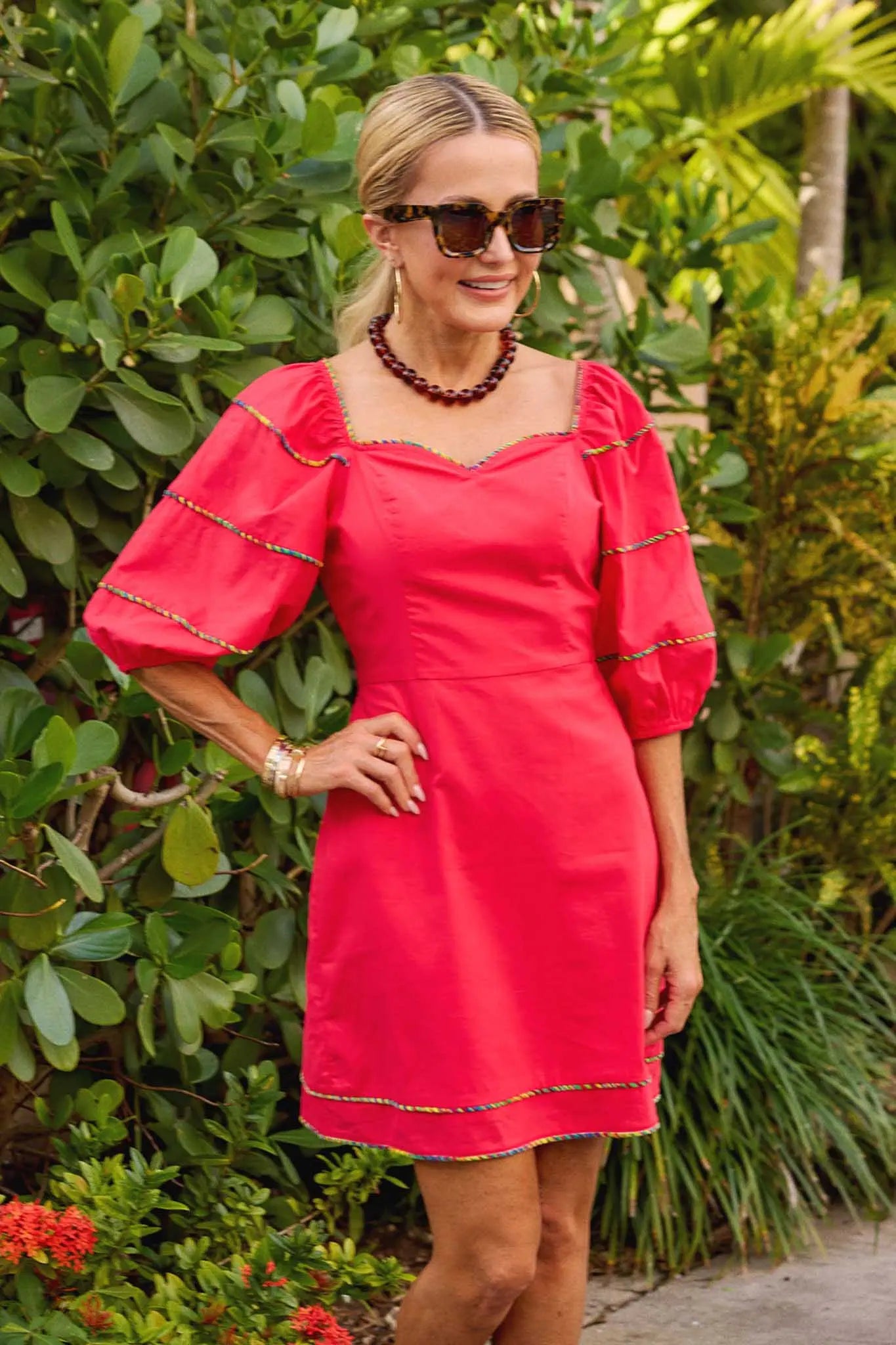 Woman wearing a red dress with gold trim standing in a garden.