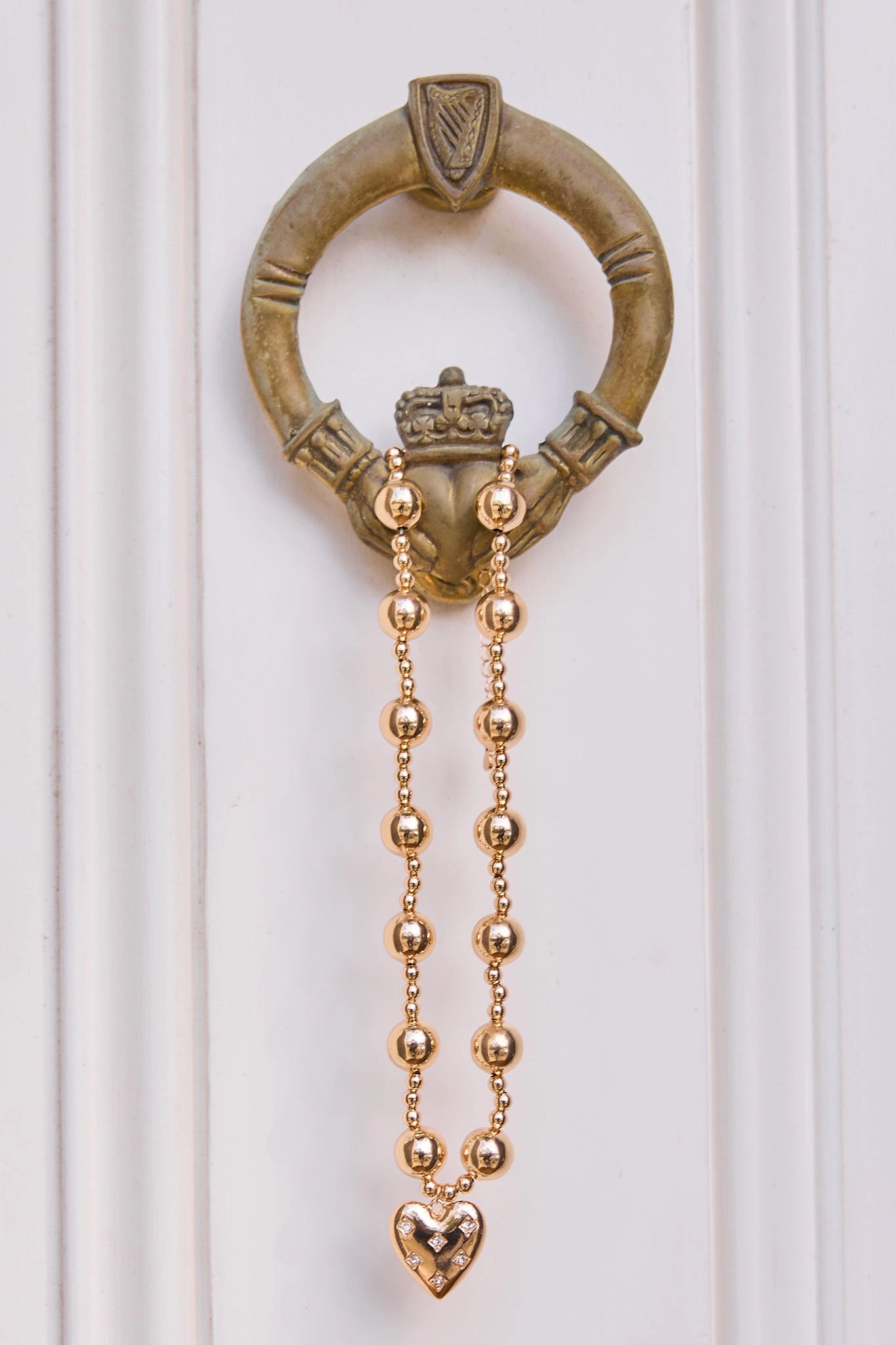 Decorative door knocker with gold chain and heart detail on a white background