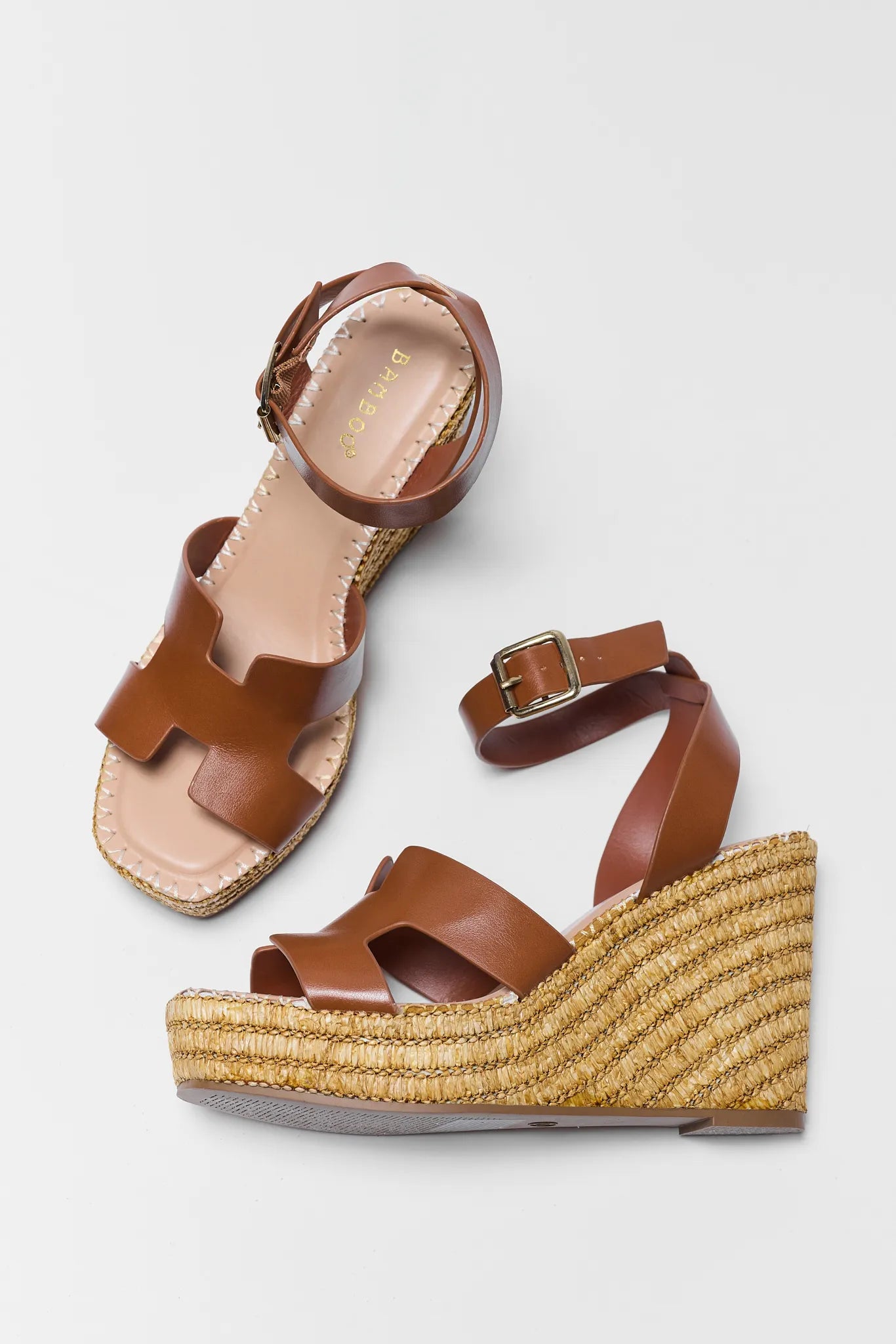 Brown wedge sandals with raffia sole on a light gray background