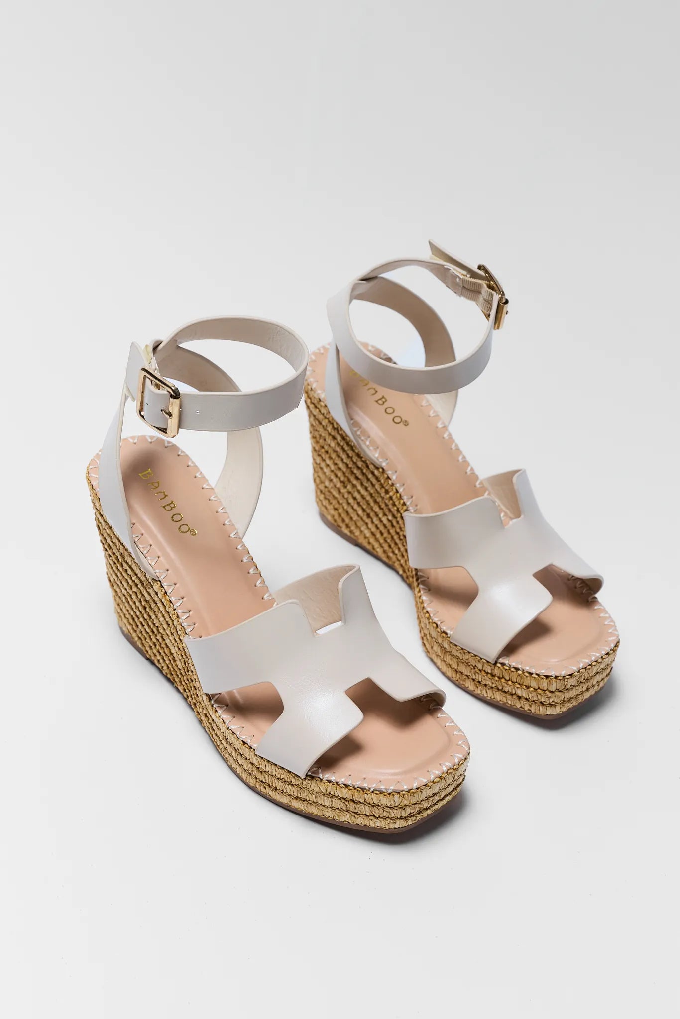 White wedge sandals with espadrille sole on a light gray background