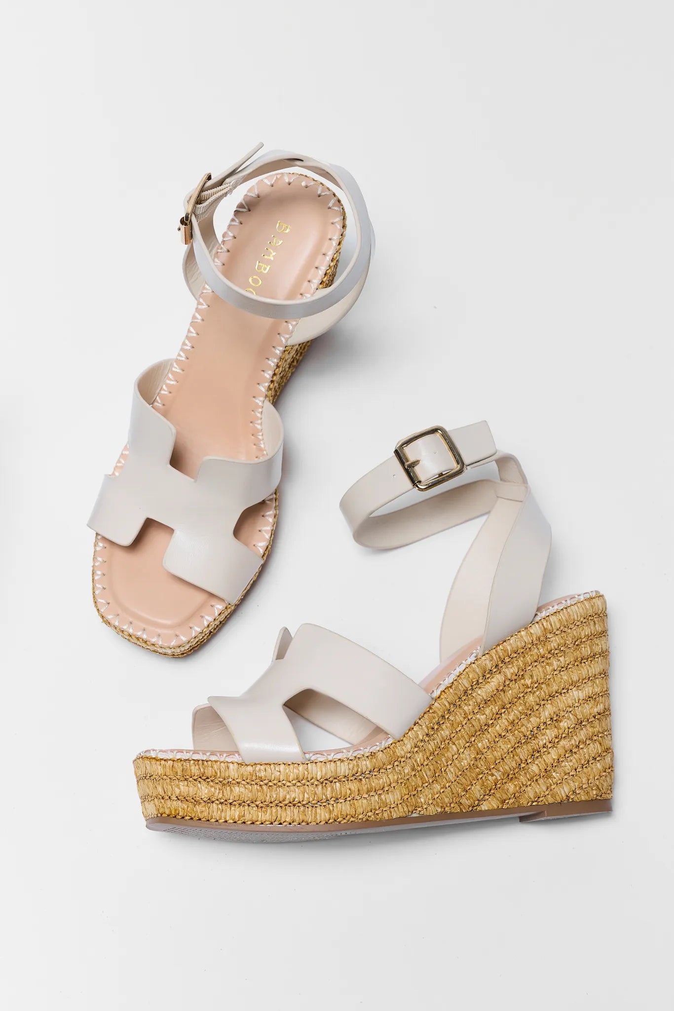 White wedge sandals with gold espadrille soles on a light gray background