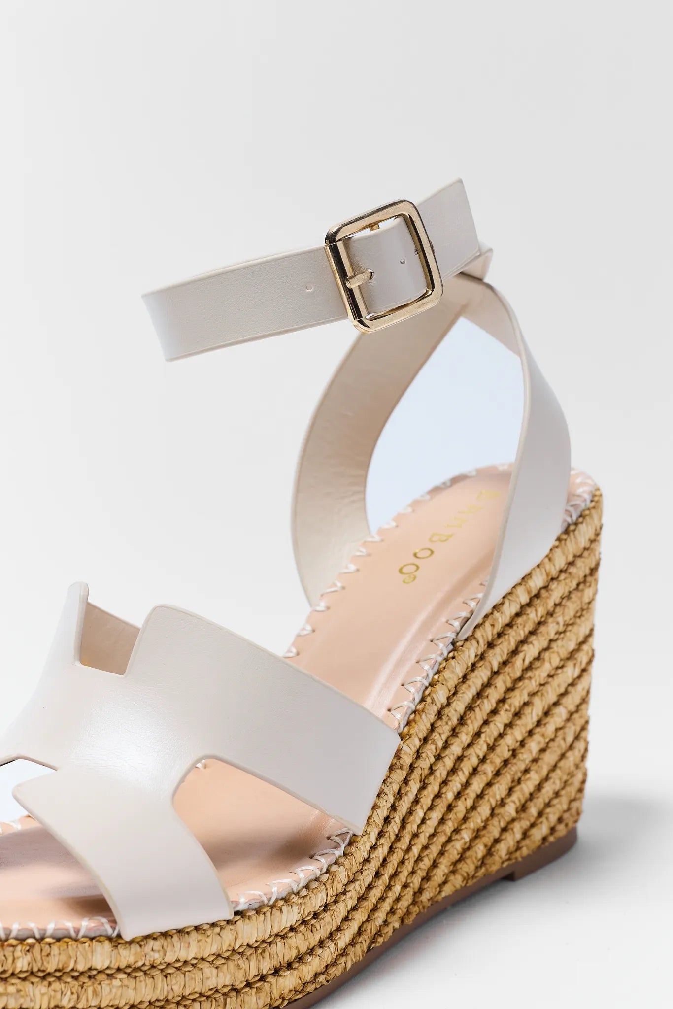 White wedge sandal with a gold buckle on a light gray background