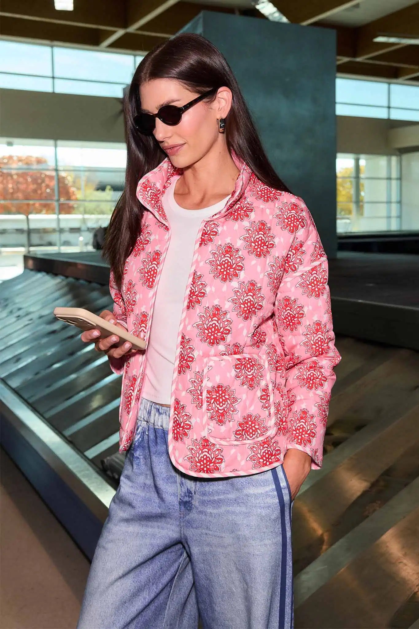 Woman in a pink floral jacket and blue jeans standing in an airport.