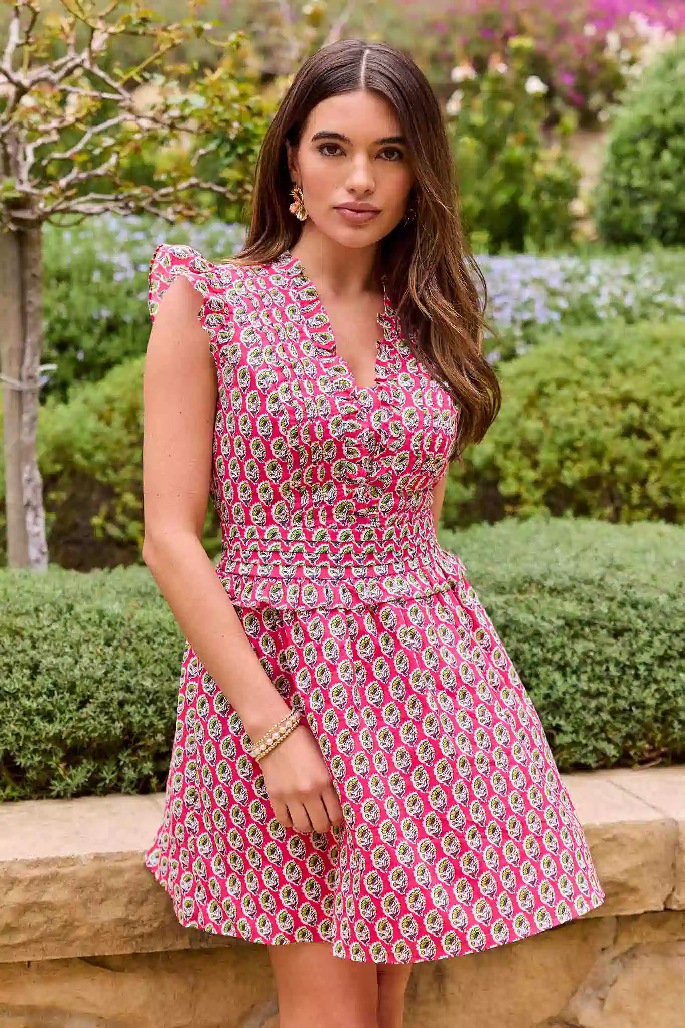 Woman wearing a pink floral dress standing outdoors with greenery in the background
