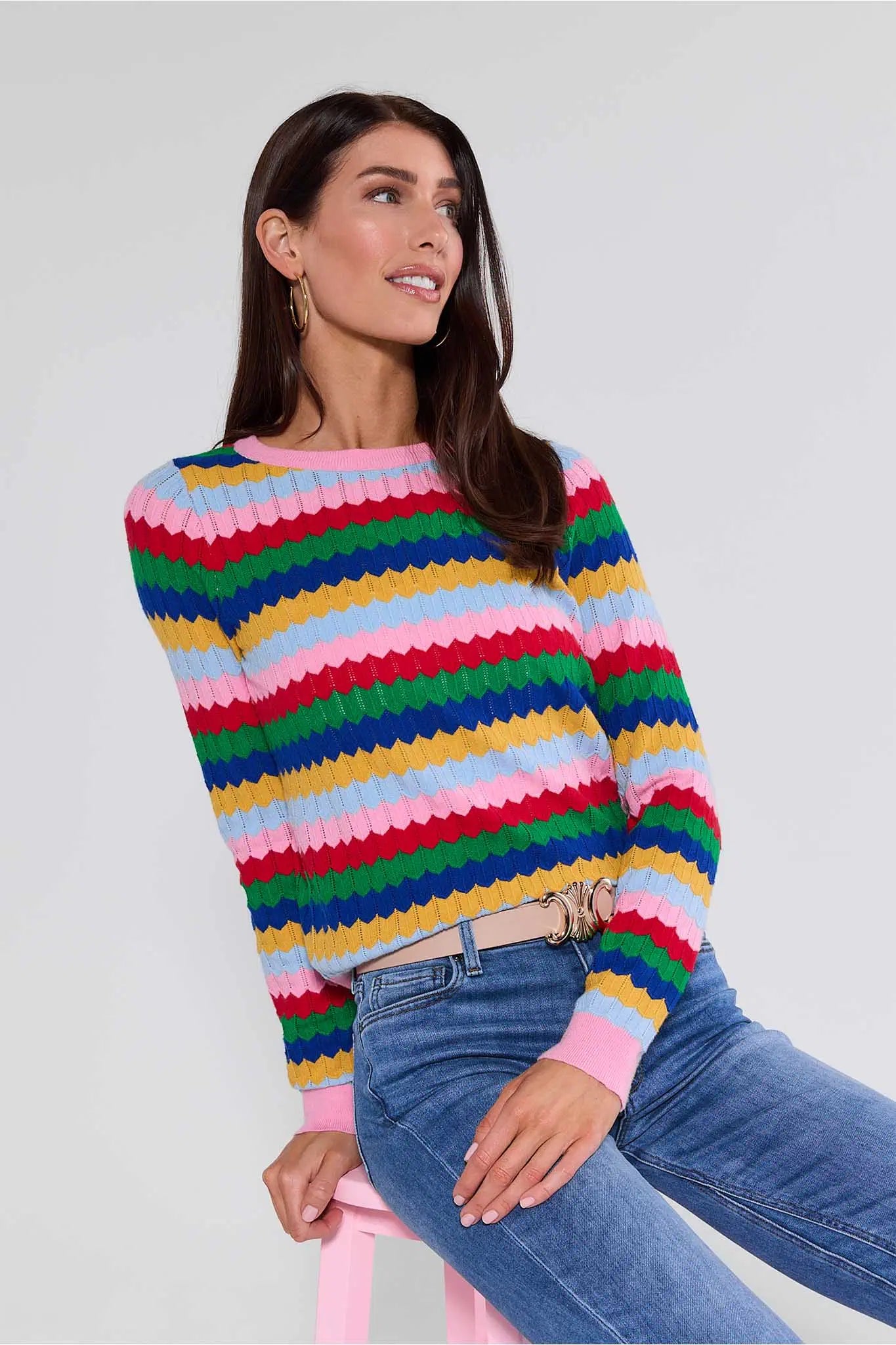 Woman wearing a colorful striped Mandy sweater and blue jeans against a plain background