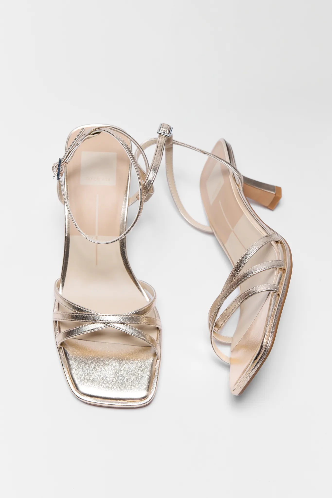 Pair of high-heeled sandals with metallic finish on a light gray background