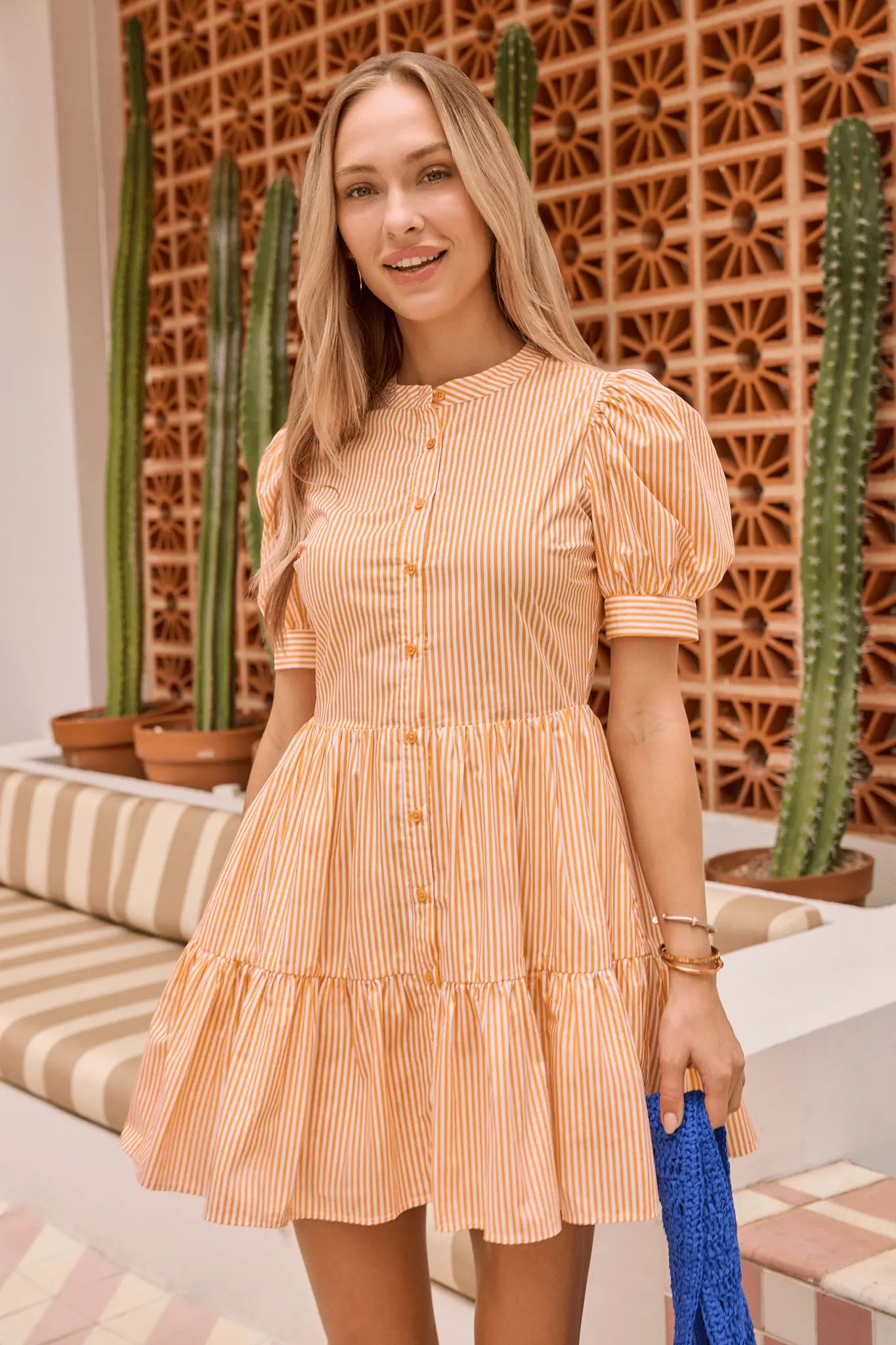 Woman in a peach striped dress standing in front of a decorative wall with cacti. lifestyle