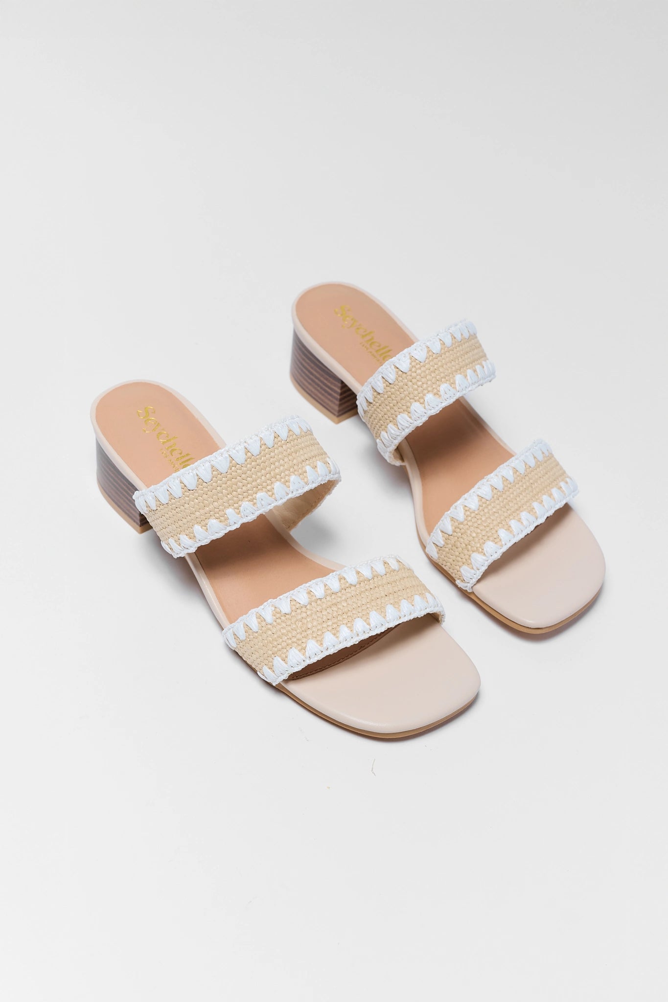 two Pair of beige sandals with white pom-pom details on a light gray background