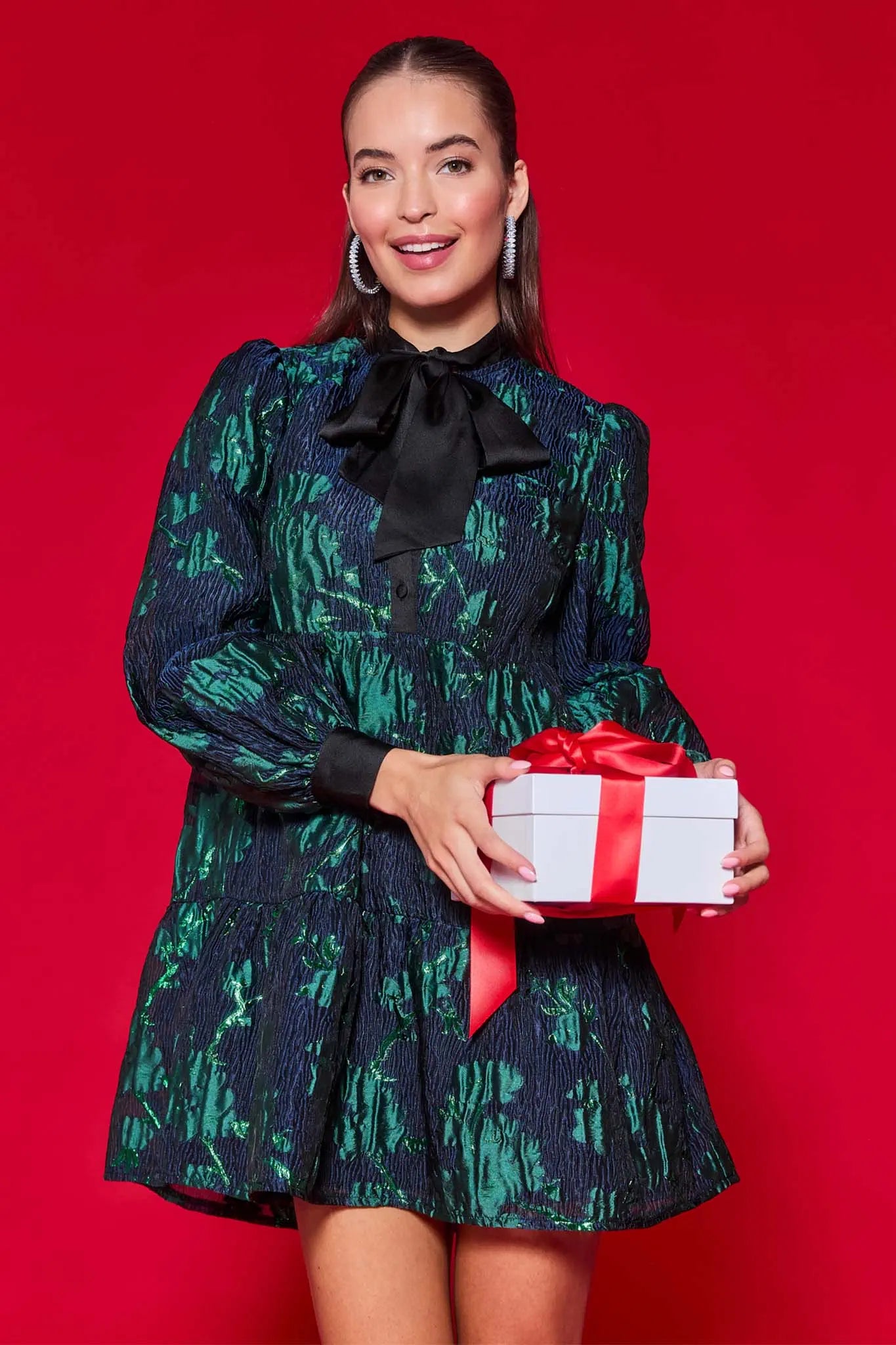 Woman wearing a dark green patterned melissa dress on a red background