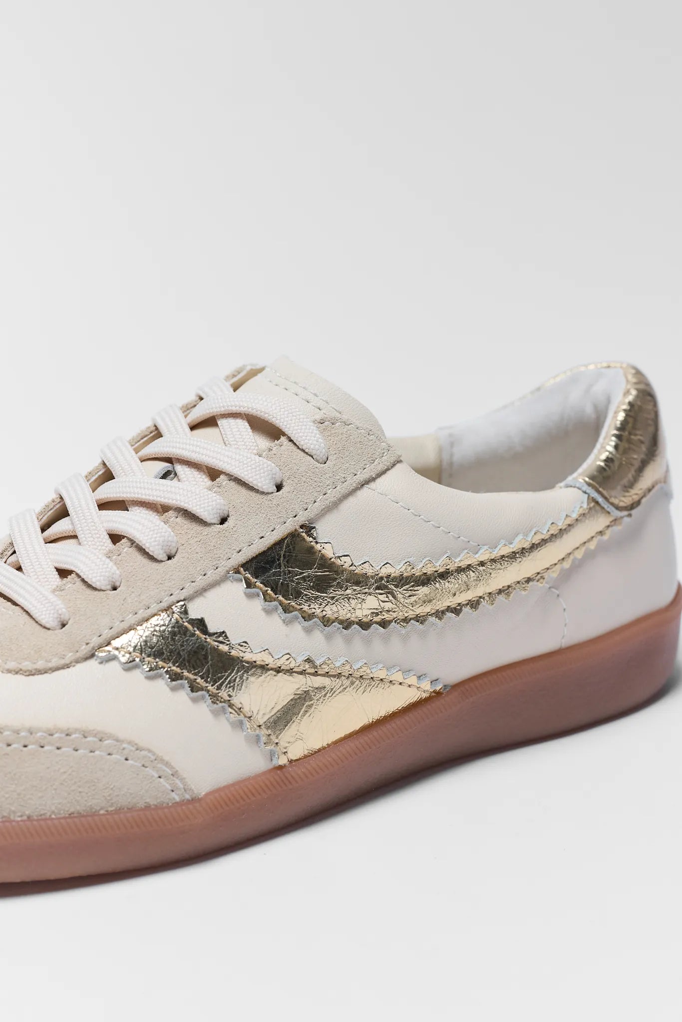 White sneaker with gold accents on a light gray background