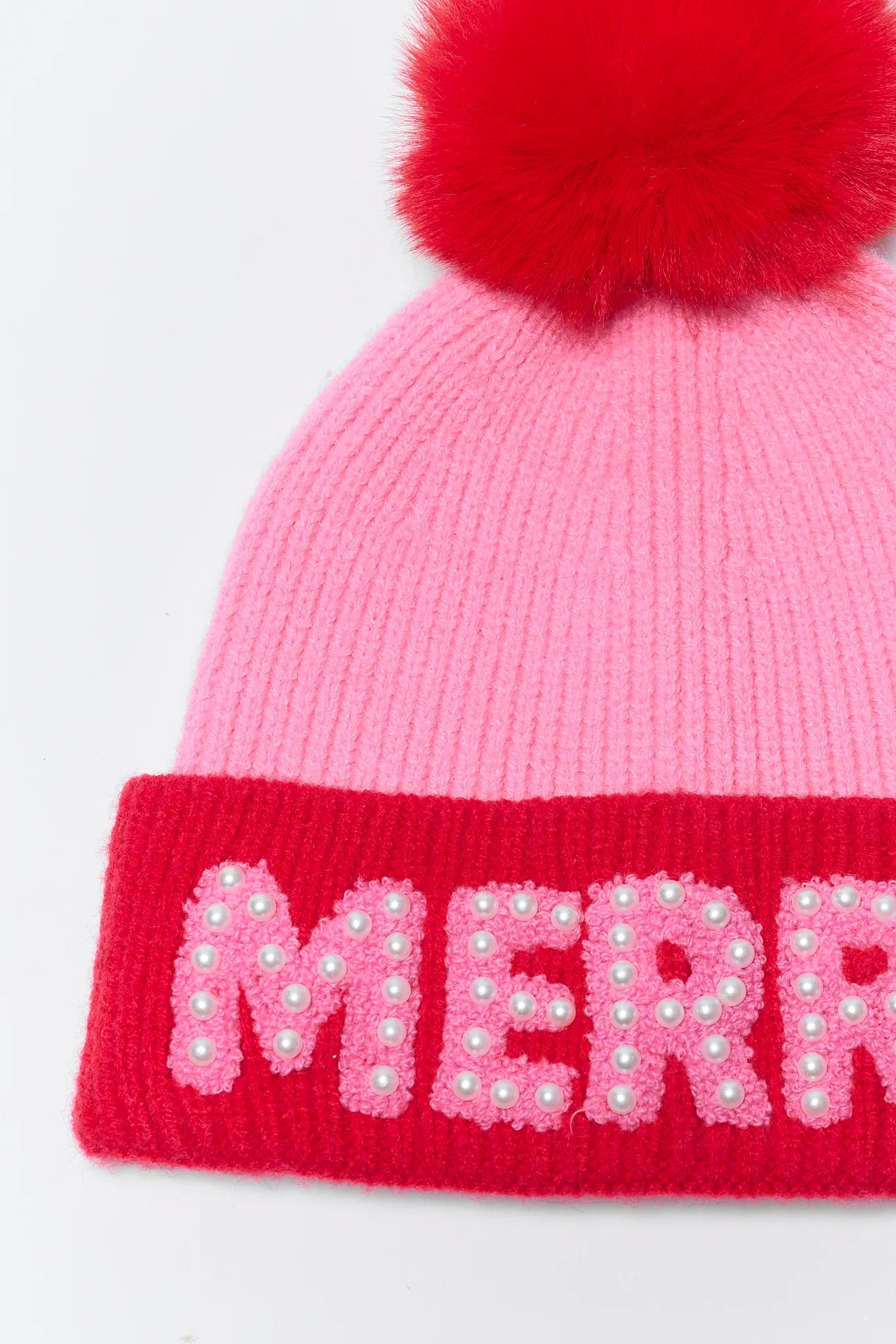 Pink knit beanie with red pom-pom and 'MERRY' in pink letters on a white background